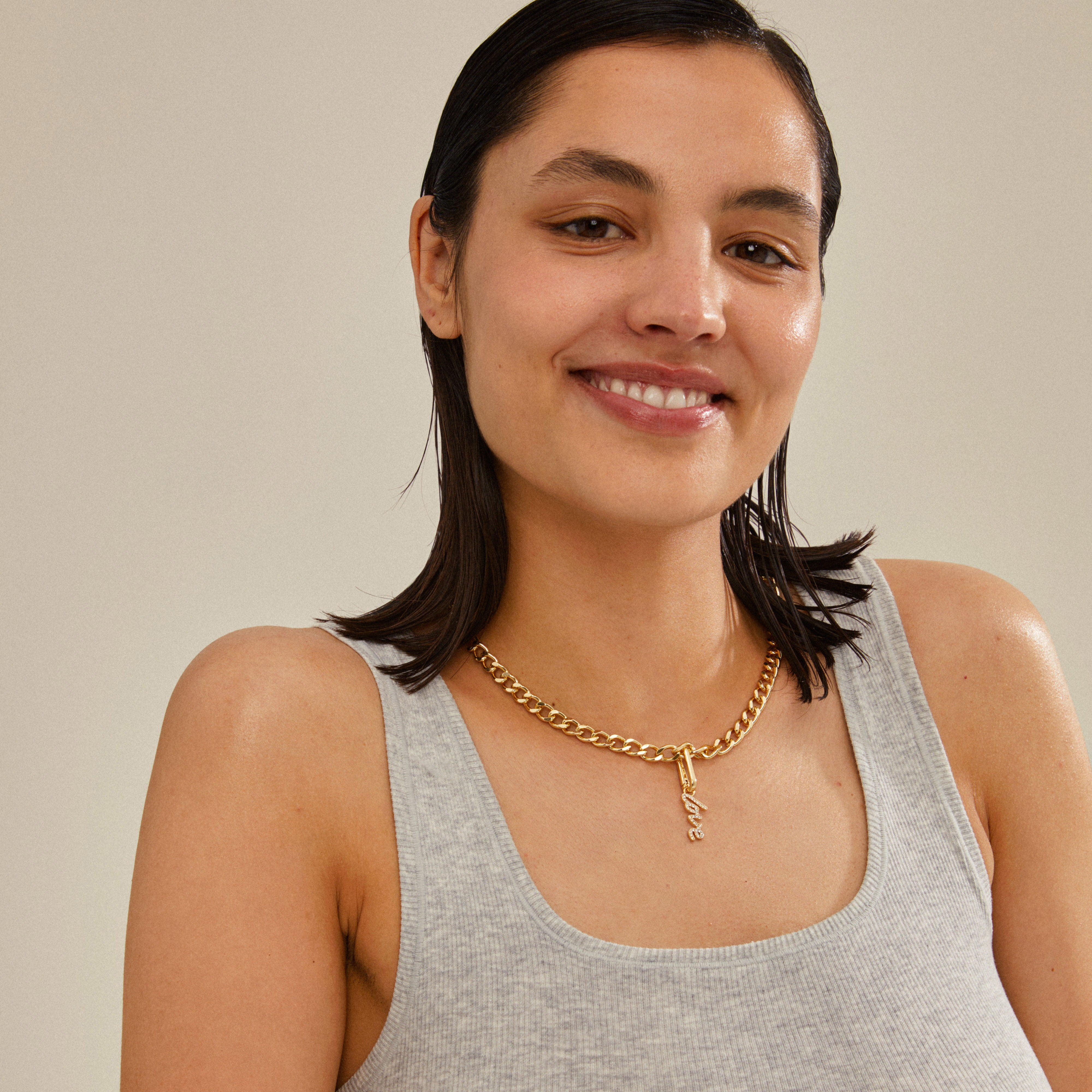 Woman smiling, wearing Pilgrim's CHARM love pendant, gold-plated, showcasing a personal, stylish touch with recycled material, perfect for trendy, personalized styling.