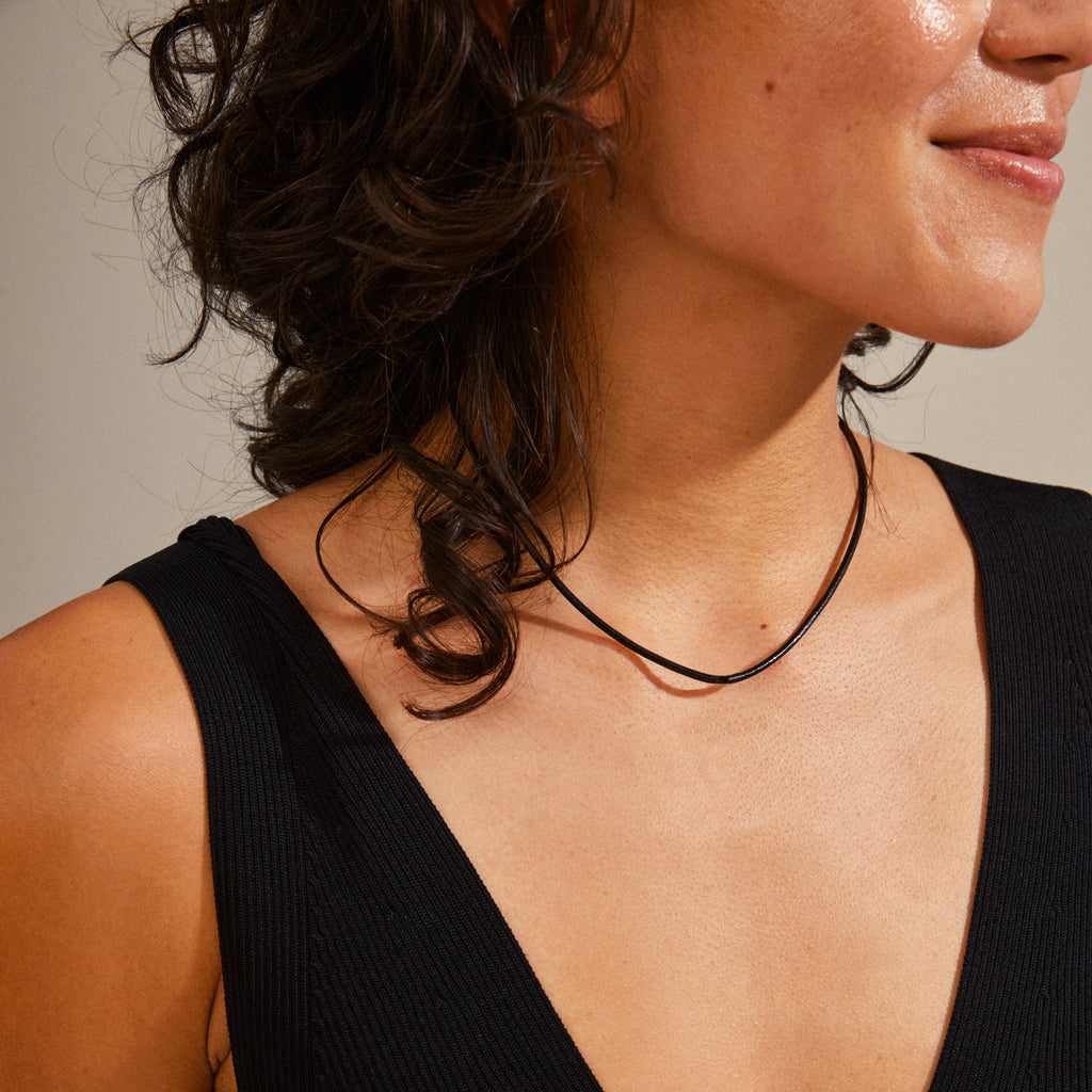 Close-up of a woman's neck wearing the CHARM leather cord necklace, featuring a black leather cord and gold-plated extension chain for customizable styling.