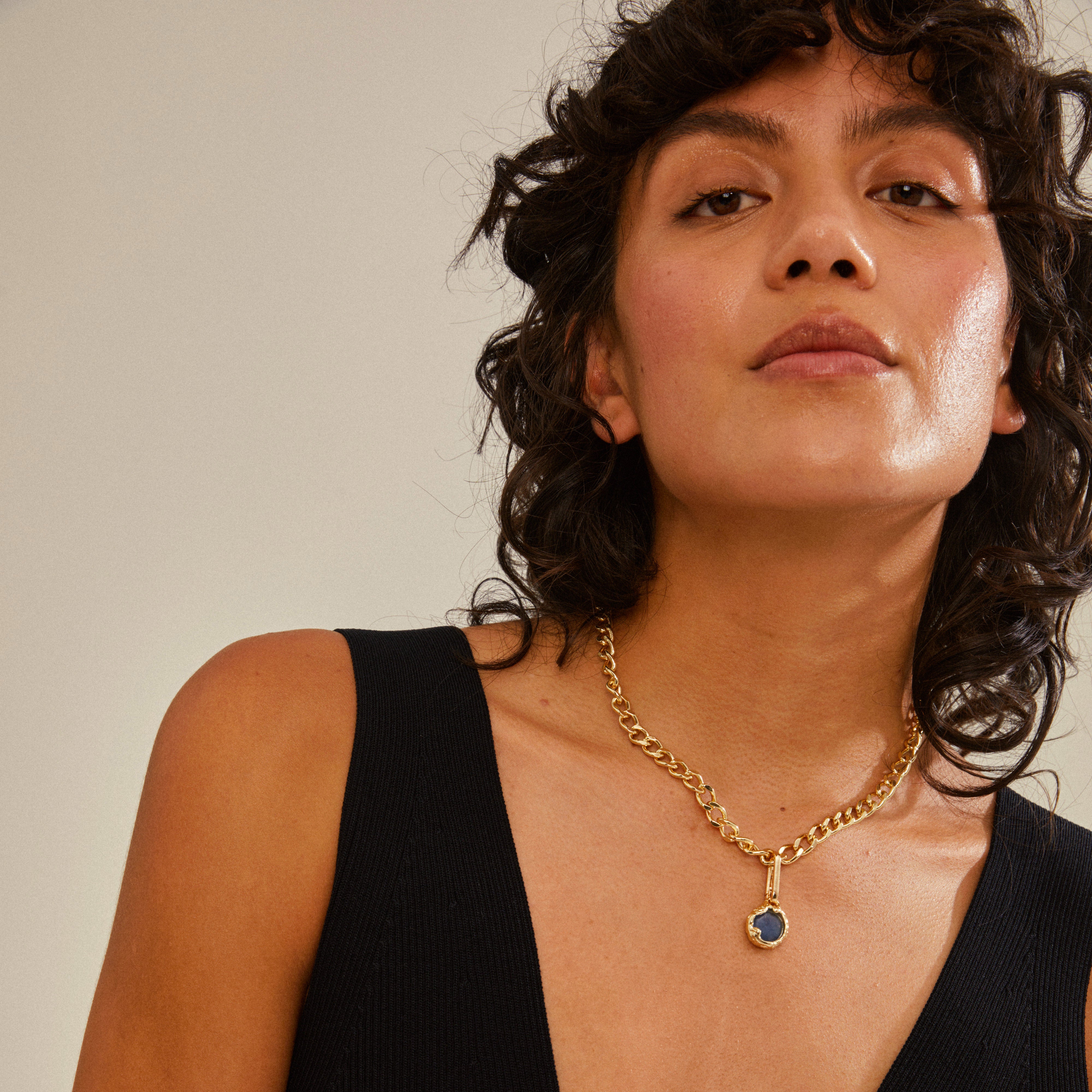 Woman wearing a black dress and a gold-plated necklace featuring a blue composite stone, showcasing Pilgrim's CHARM natural pendant for a trendy, personalized style.