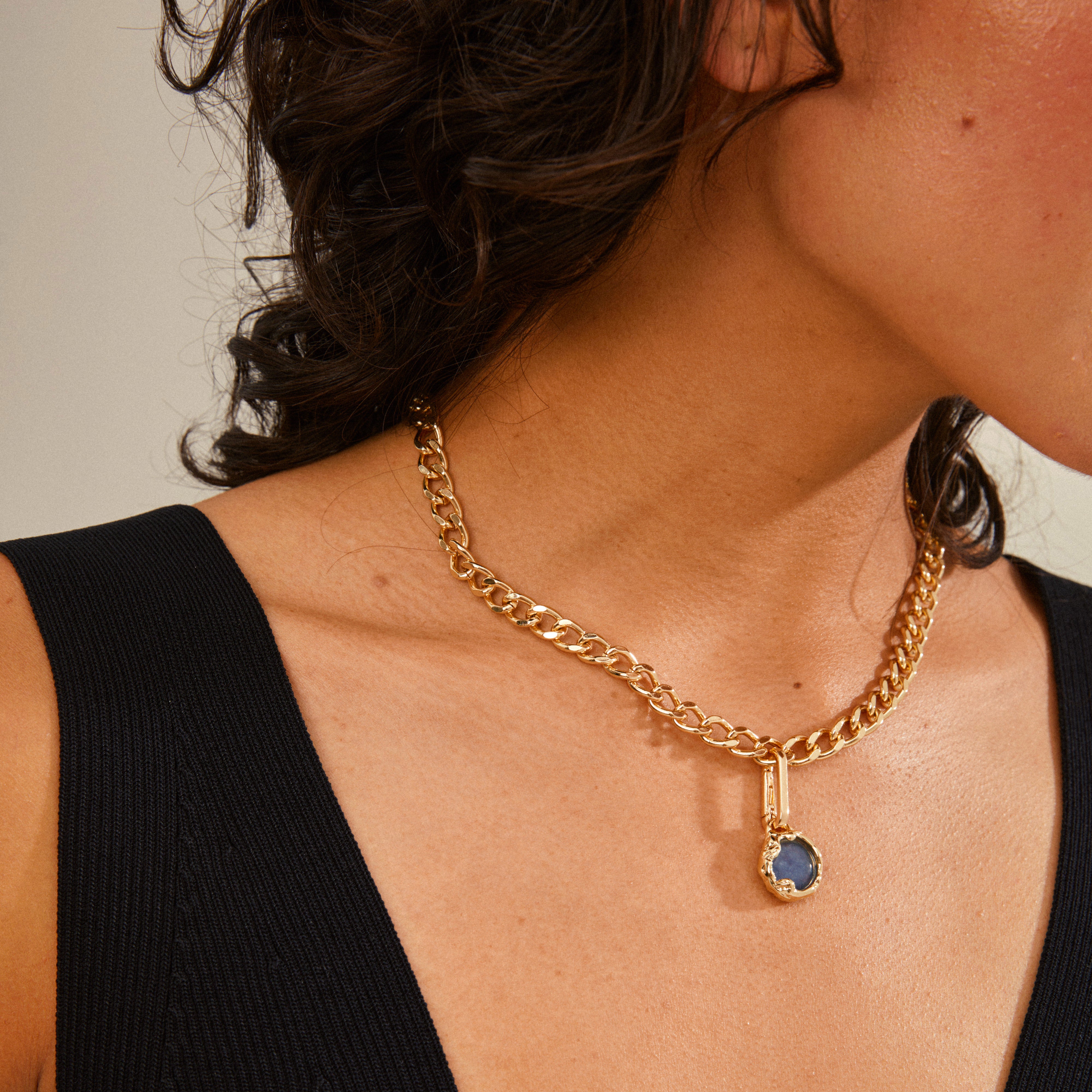 Woman wearing the CHARM natural pendant, blue/gold-plated, featuring a gold pendant with a blue stone from Pilgrim, highlighting timeless Danish jewelry craftsmanship.