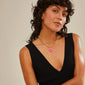 Woman with curly hair wearing a black dress showcases Pilgrim's CHARM heart pendant, pink/gold-plated, highlighting its unique, personalized design ideal for personal style expression.