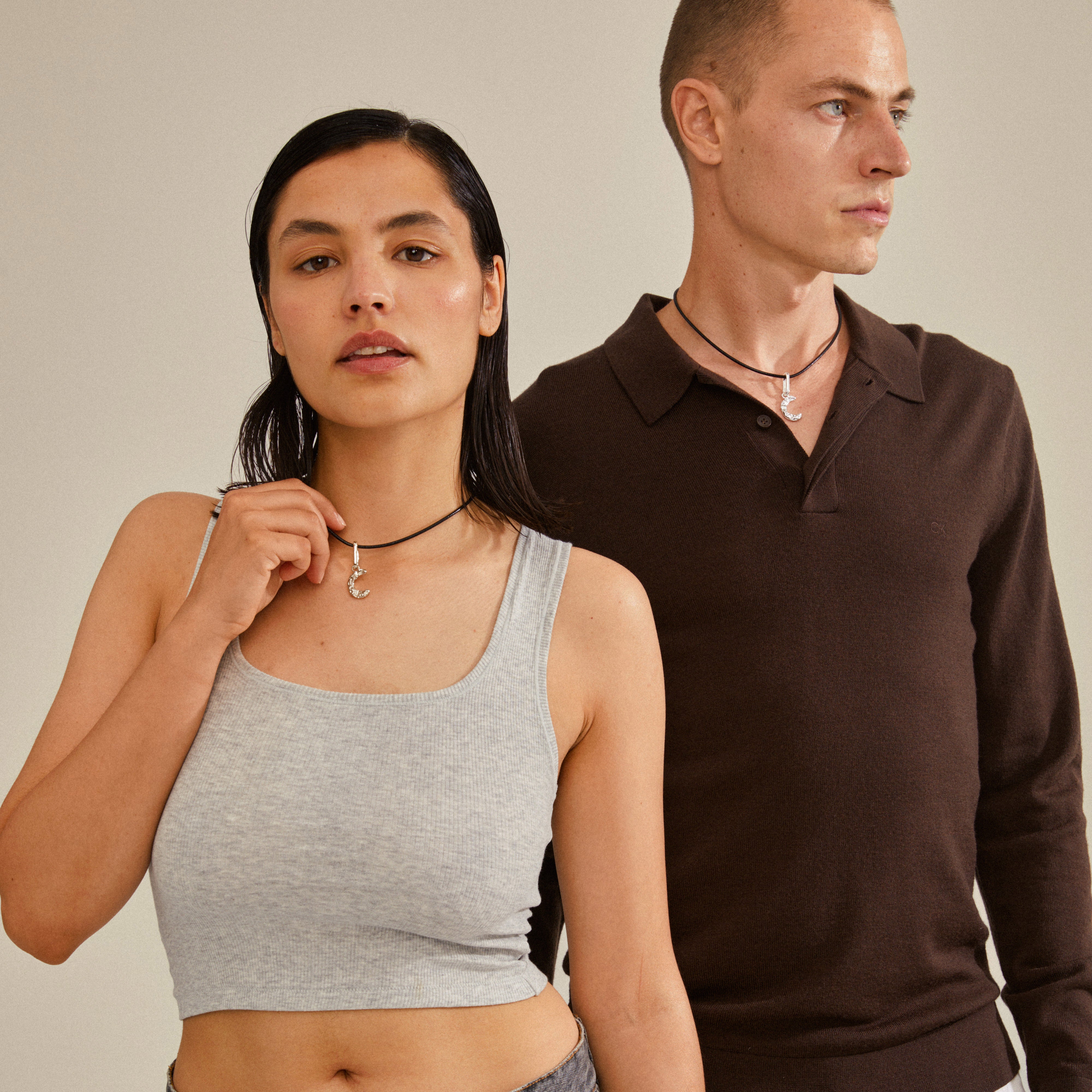 Man and woman showcasing Pilgrim's CHARM pendant C, silver-plated, designed for personal style with recycled material, highlighting Scandinavian craftsmanship and individuality.