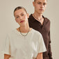 Man and woman showcasing Pilgrim's CHARM pendant E, silver-plated, highlighting its personalized style and recycled material. Both wear the necklace elegantly, reflecting Scandinavian design.