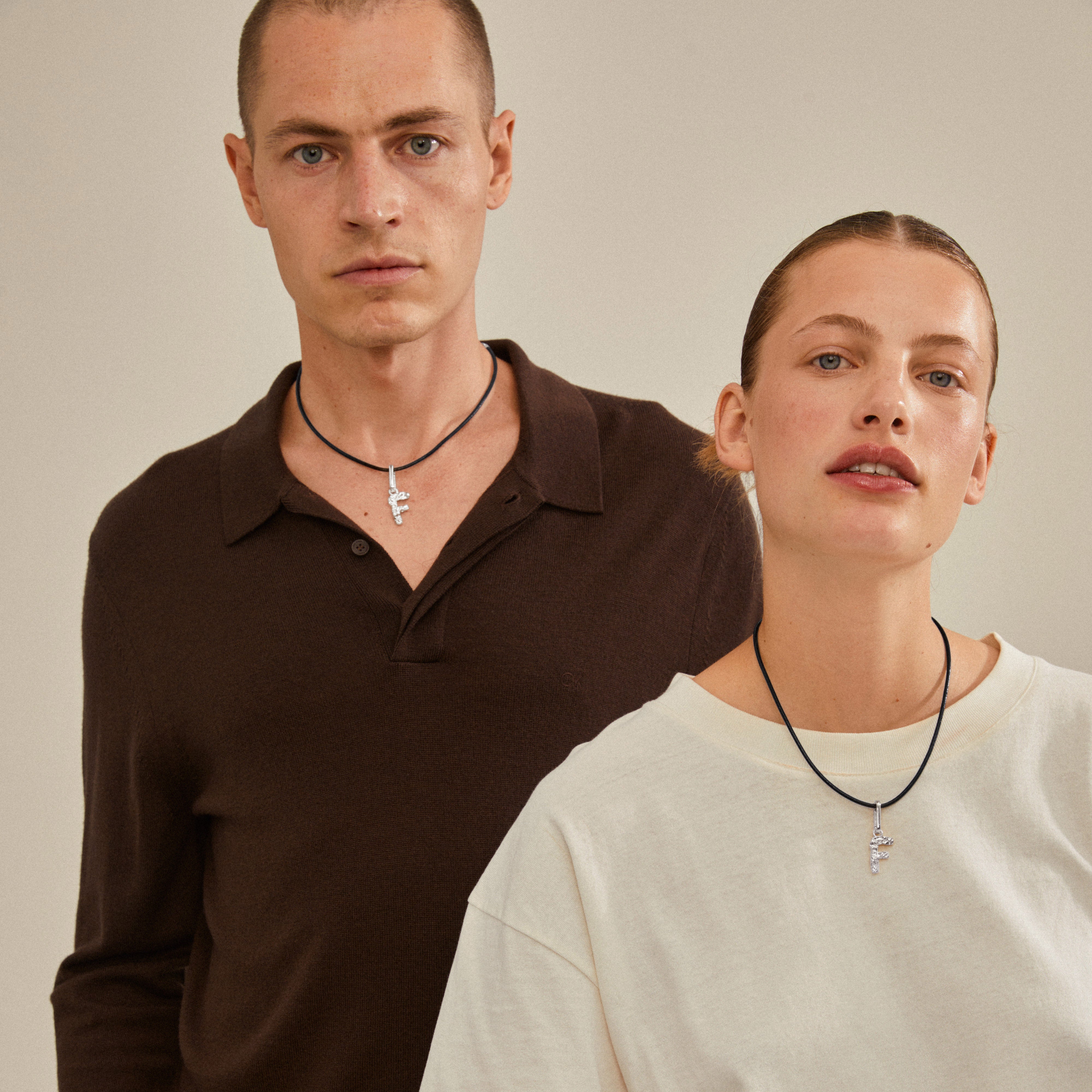 Man and woman showcasing a CHARM pendant F, silver-plated, from Pilgrim, worn on necklaces, emphasizing personalized and sustainable fashion.
