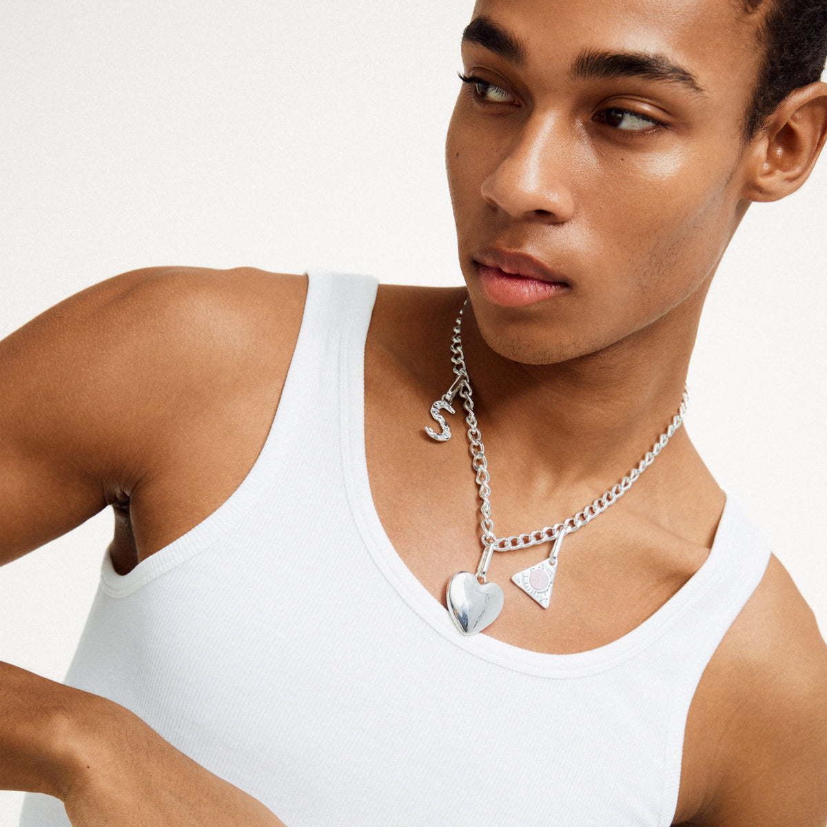 Man wearing a white tank top showcases Pilgrim's CHARM pendant S, silver-plated, emphasizing its customizable, eco-friendly design for personalized style.