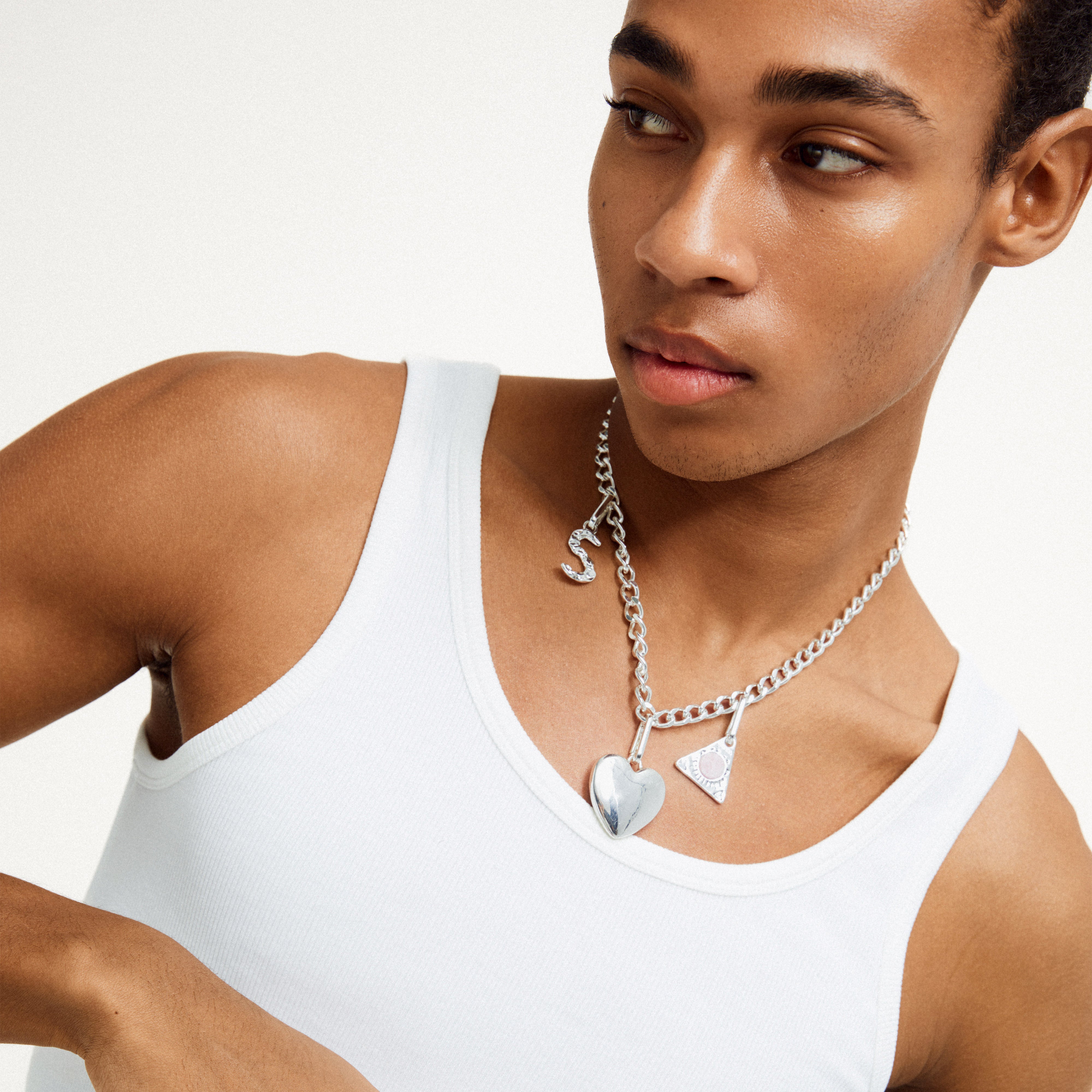 Man wearing a white tank top showcases Pilgrim's CHARM pendant S, silver-plated, emphasizing its customizable, eco-friendly design for personalized style.