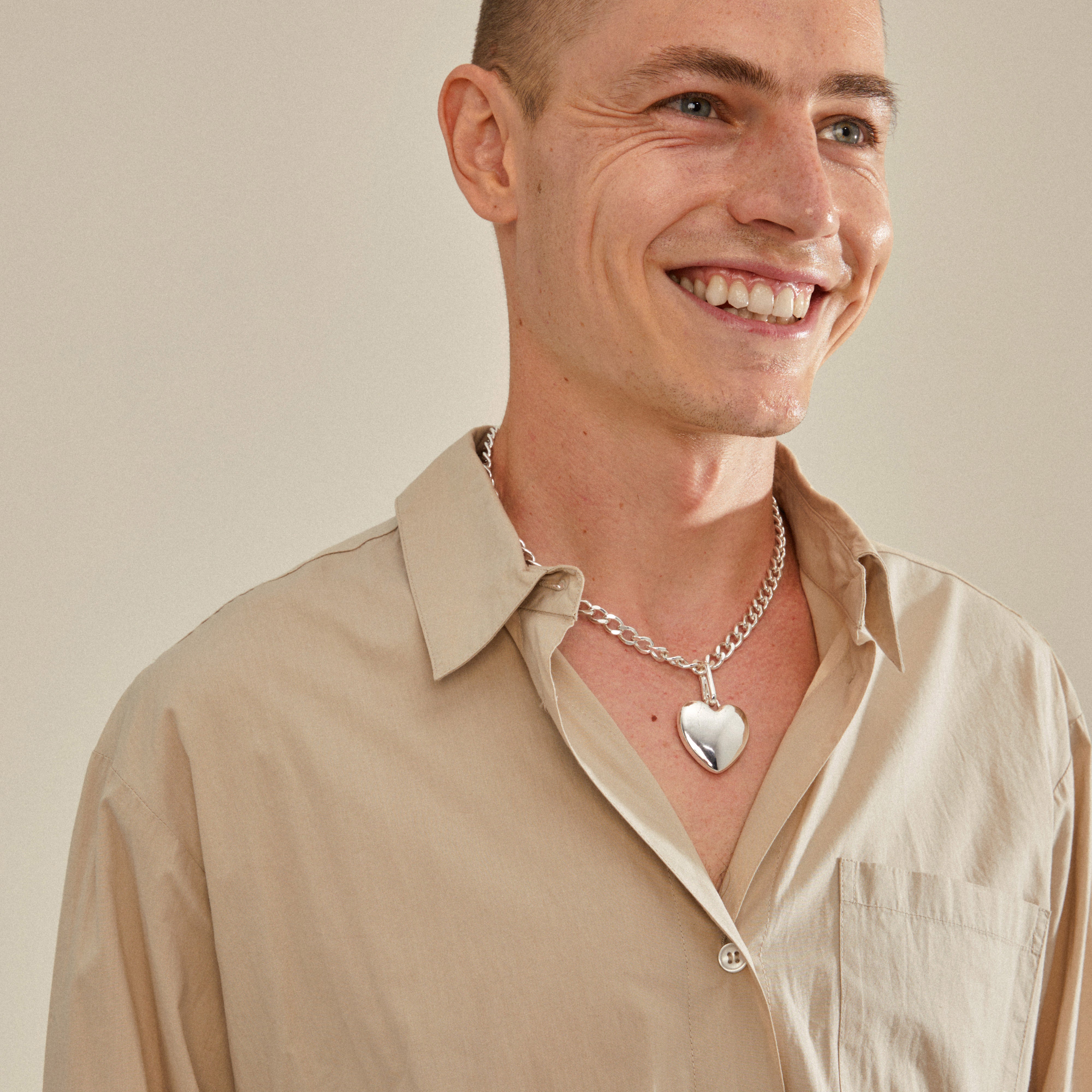 Man smiling, wearing Pilgrim's CHARM maxi heart pendant, silver-plated, showcasing a stylish, recycled accessory perfect for personalized fashion statements.