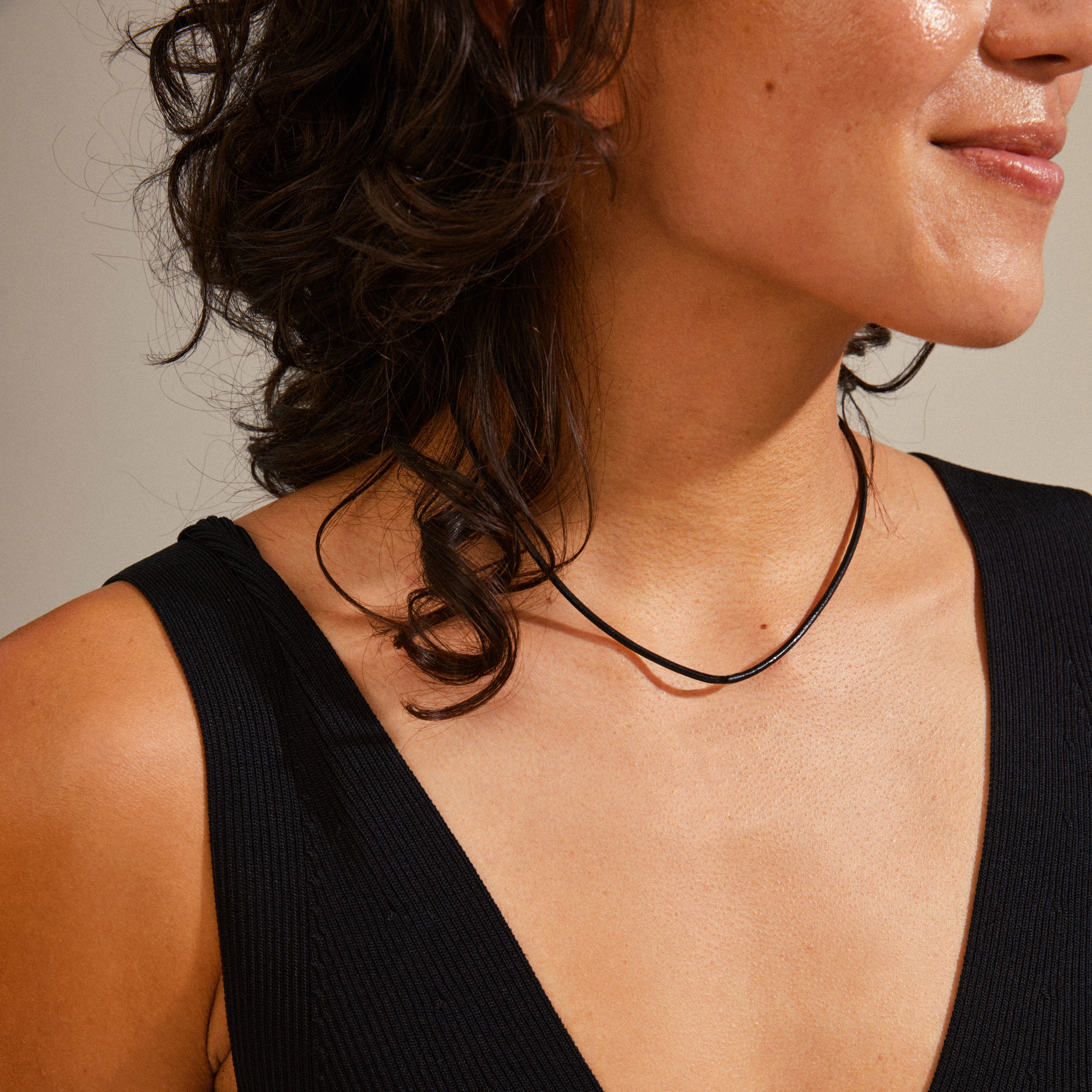 Close-up of a woman wearing the CHARM leather cord necklace, featuring a simple black cord with a silver-plated extension chain for charm customization.