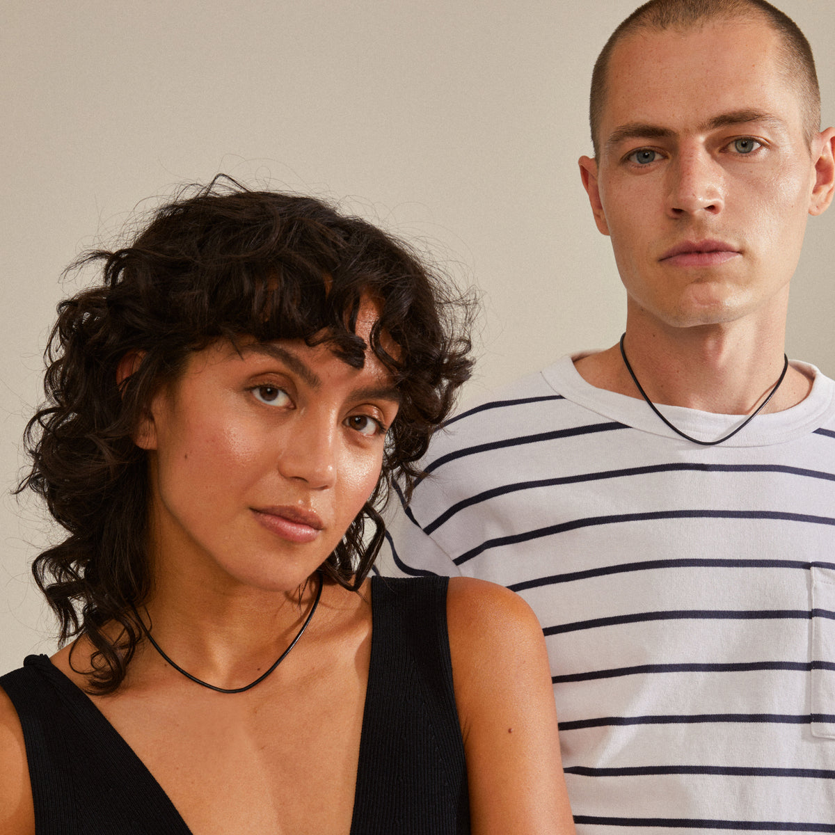 Man and woman showcasing the CHARM leather cord necklace, black/silver-plated, styled simply, emphasizing its adjustable length and natural, earthy appeal.