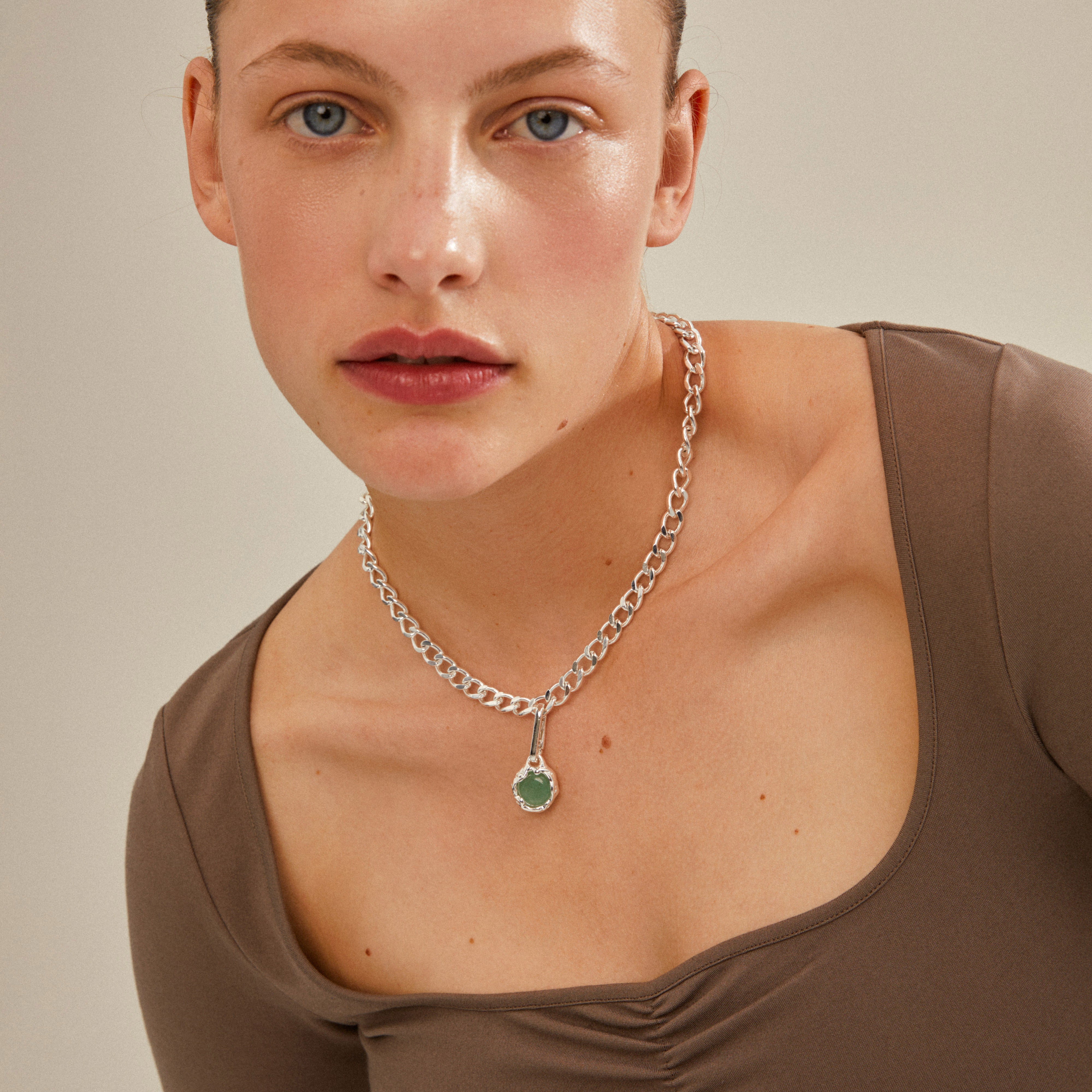 Woman wearing Pilgrim's CHARM natural pendant, green/silver-plated, featuring a prominent green stone, highlighting its unique, sustainable design for personalized style.