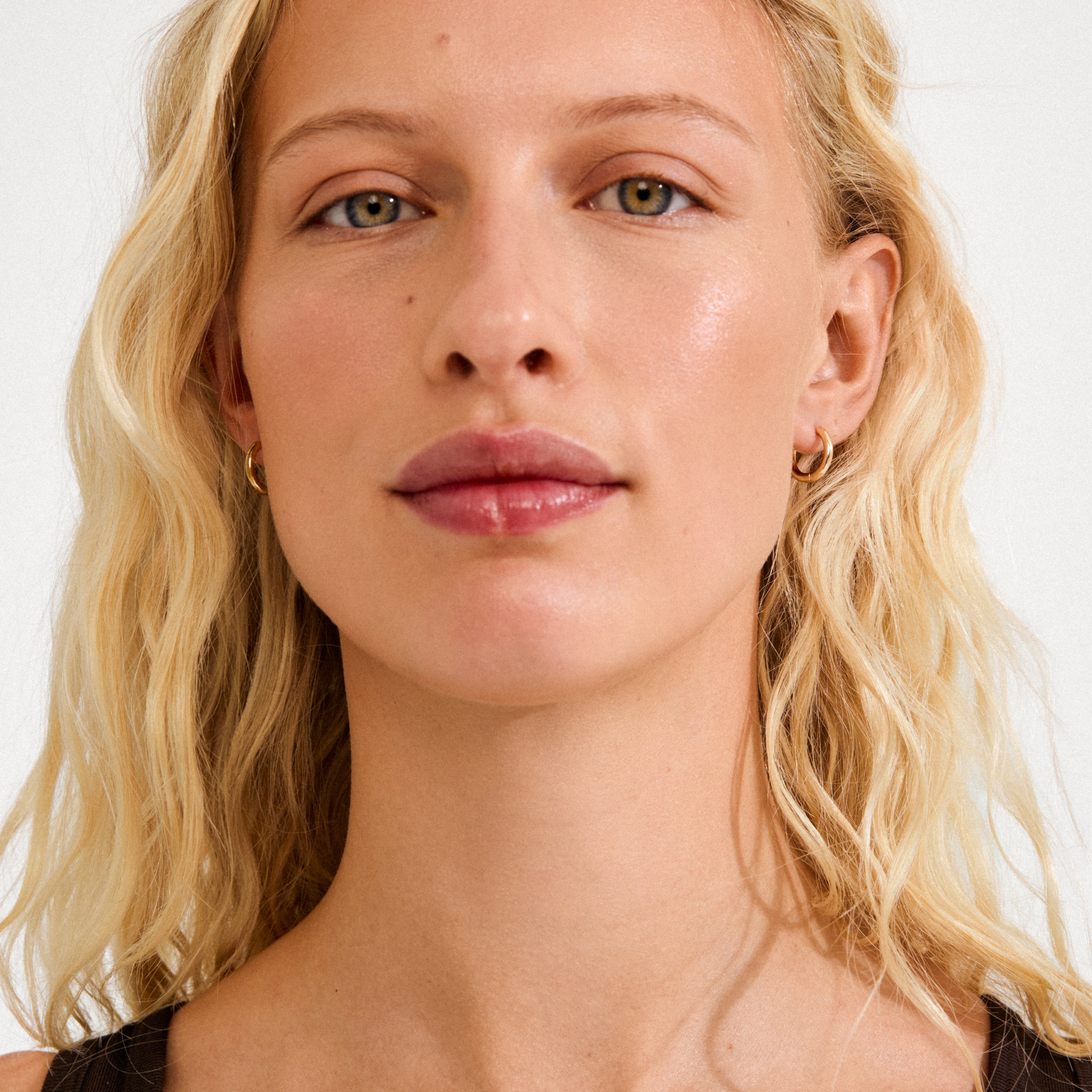 Young woman wearing CHARM small gold-plated hoop earrings, designed for adding charms, highlighting Pilgrim's blend of timeless Scandinavian craftsmanship and trendy, personal style options.