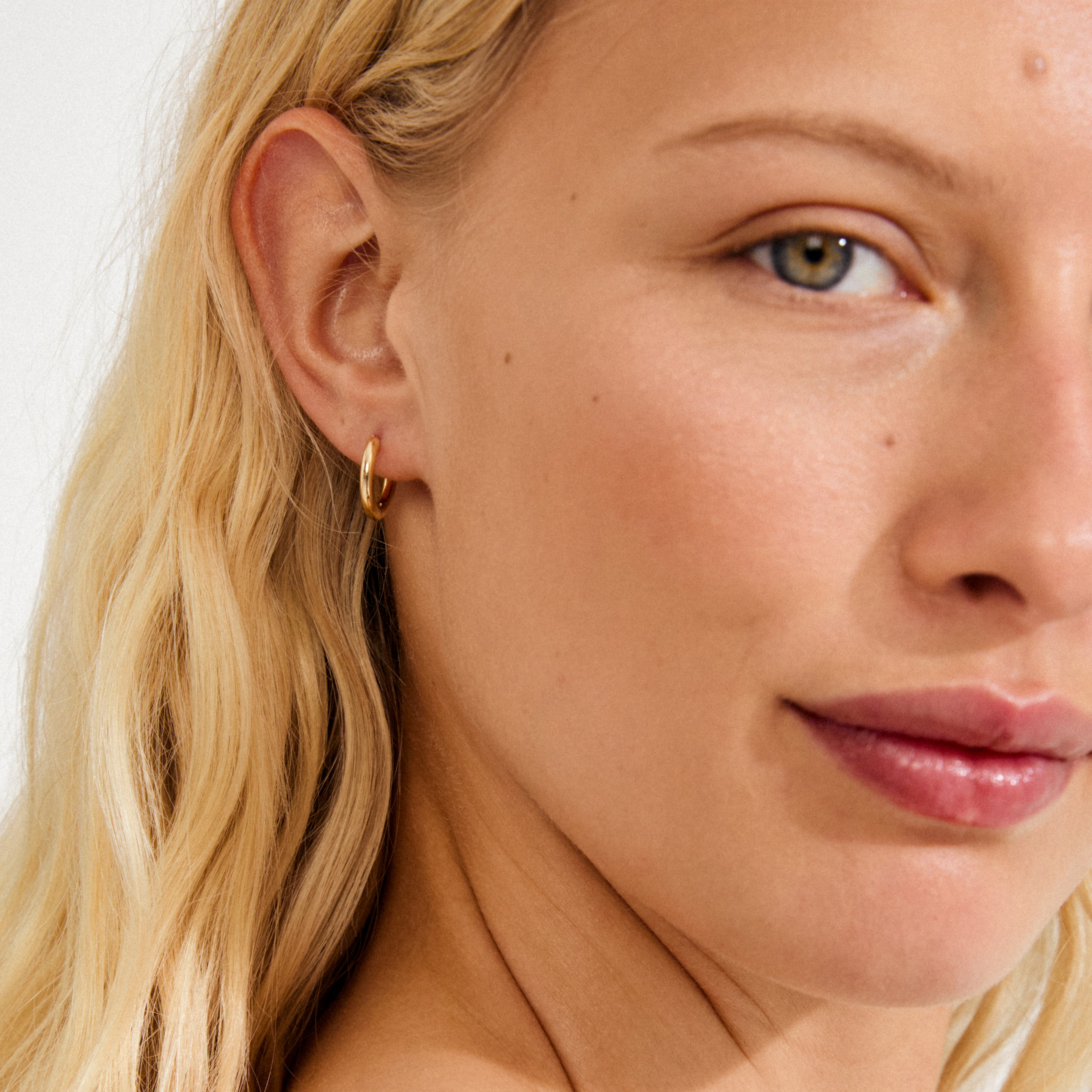 Gold-plated CHARM small hoop earring on a woman's ear, ideal for adding personalized pendants, reflecting Pilgrim's blend of timeless and trendy Danish jewelry.