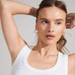 Woman modeling CHARM large hoop earrings, gold-plated, ideal for adding personalized charms. Features a 25 mm diameter, crafted from 99% recycled materials for eco-friendly fashion.