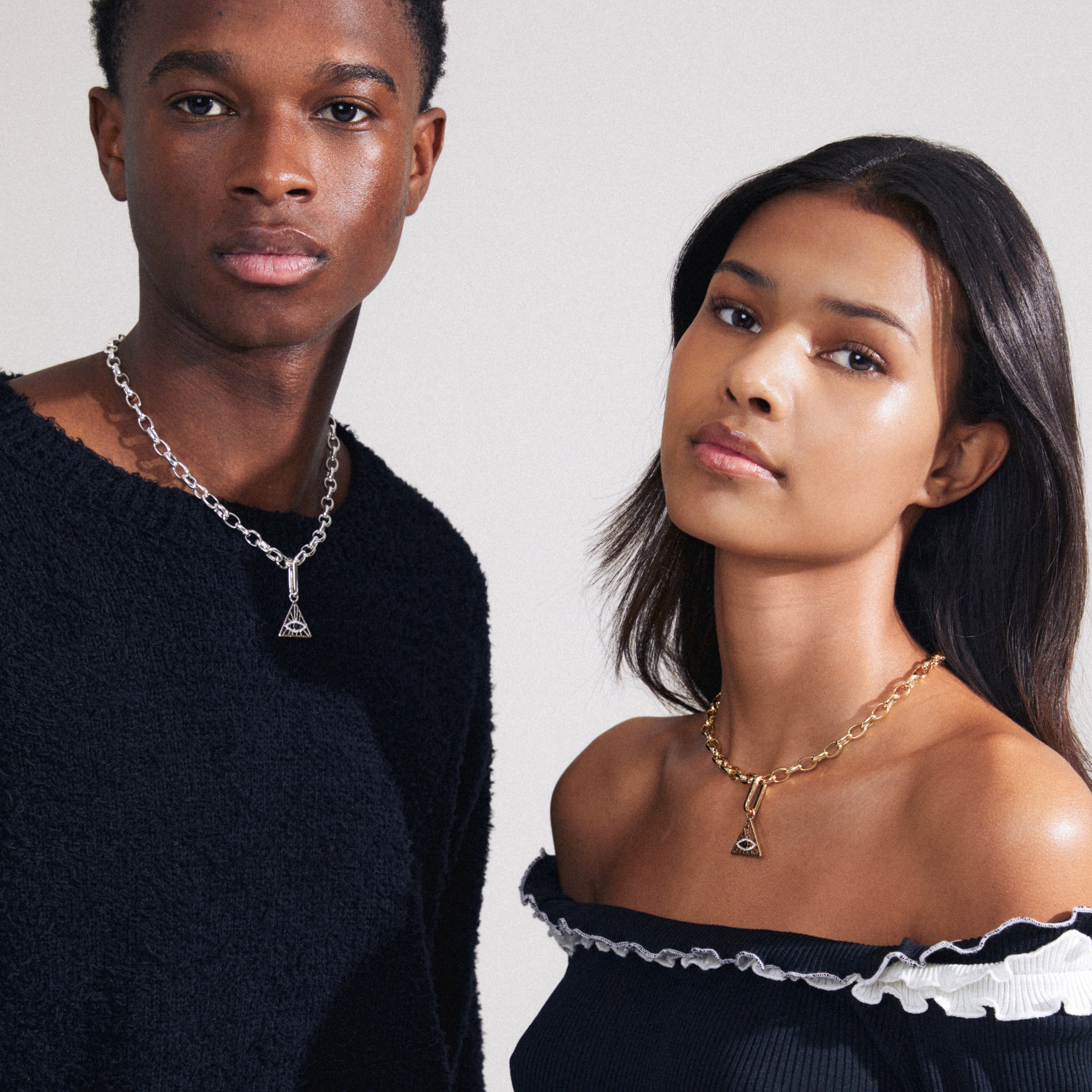 A man and woman showcase the CHARM triangle pendant, gold-plated, featuring an all-seeing eye, perfect for personalized styling with Pilgrim's recycled jewellery.