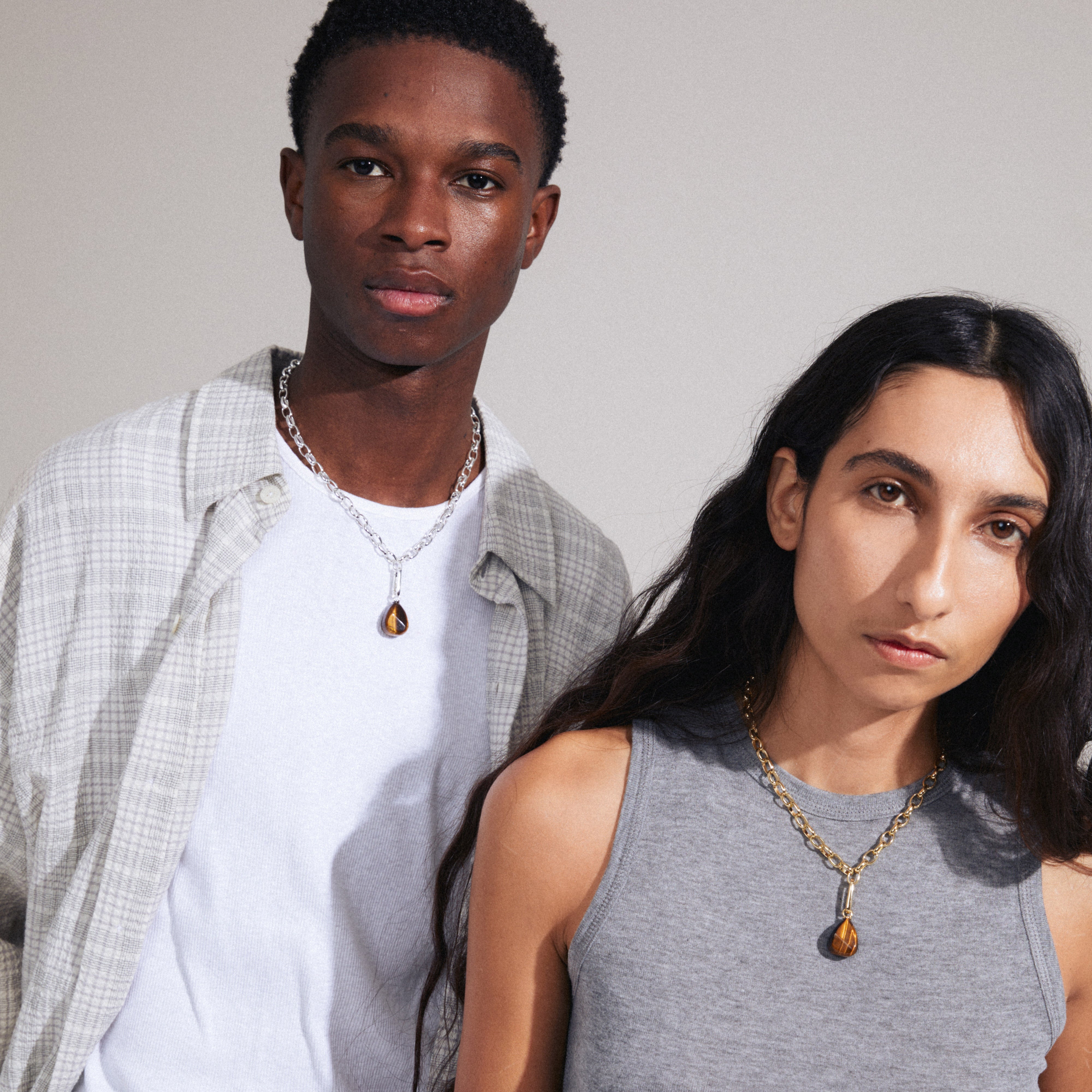 A man and woman showcase Pilgrim's CHARM tiger eye pendant, gold-plated, highlighting its versatile style and personalization options.