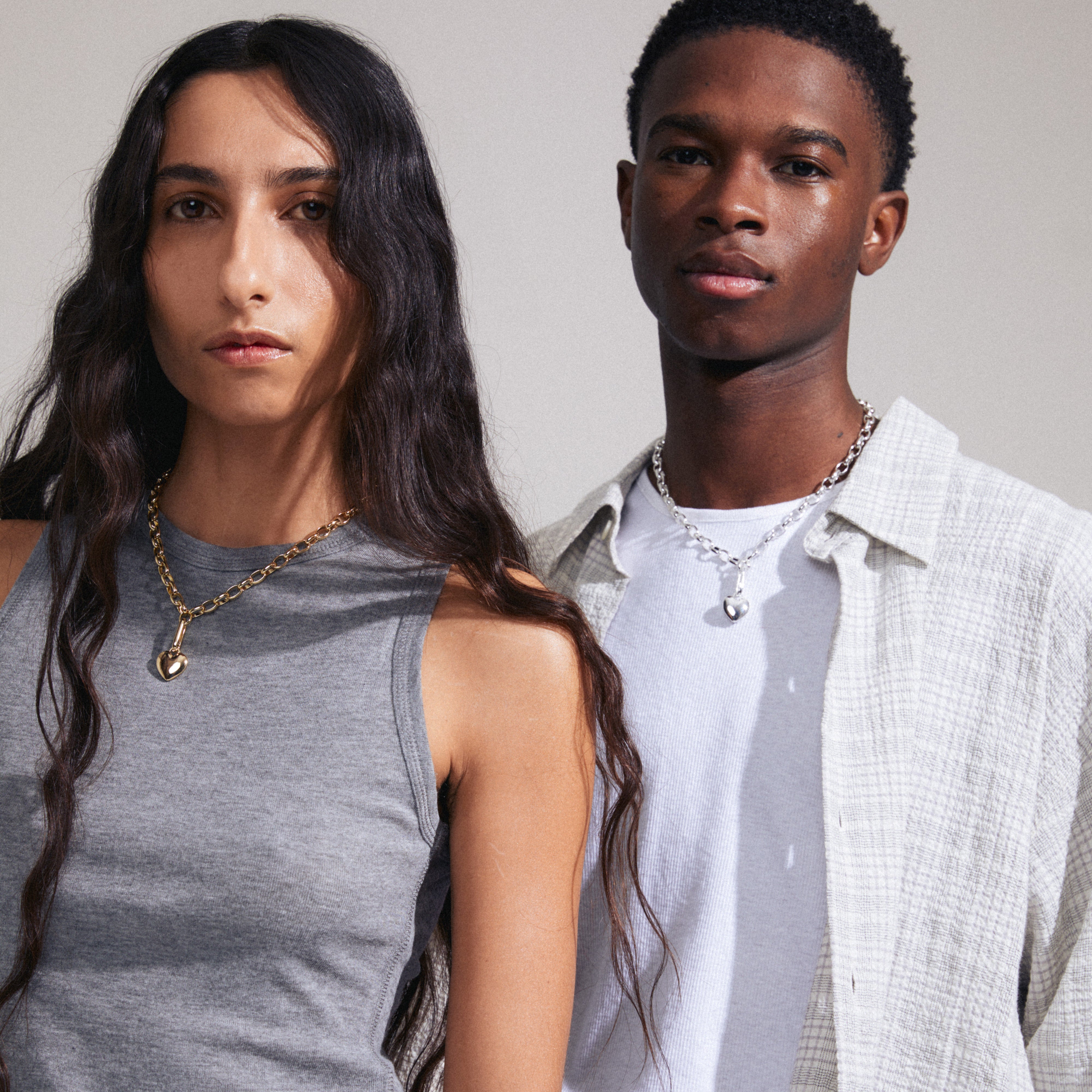 Man and woman showcasing Pilgrim's CHARM heart pendant, silver-plated, emphasizing personal style. The pendant is made from 99% recycled materials.