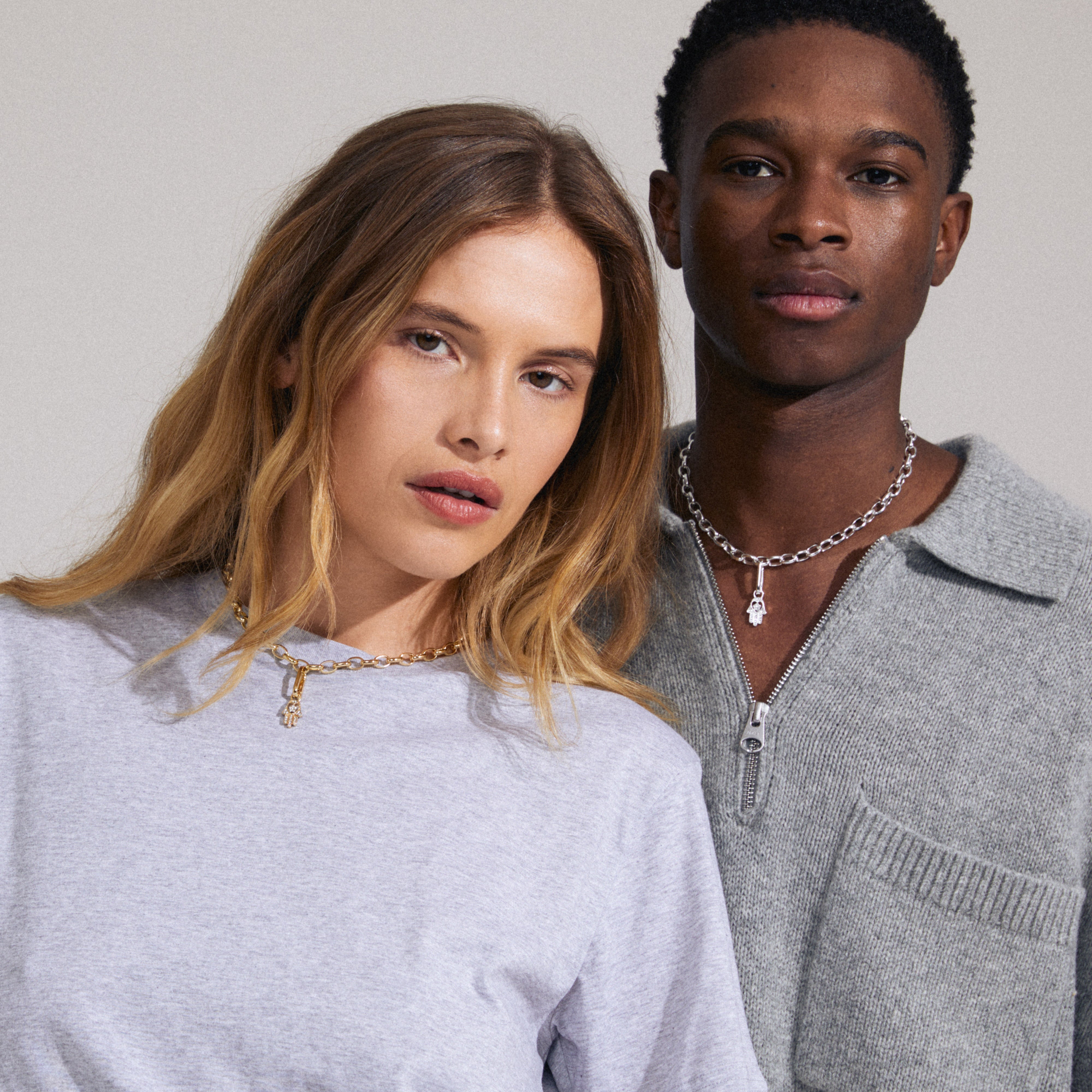 A man and woman wearing the CHARM Hamsa pendant, silver-plated, showcasing its intricate design and Preciosa crystals for a personalized style statement.