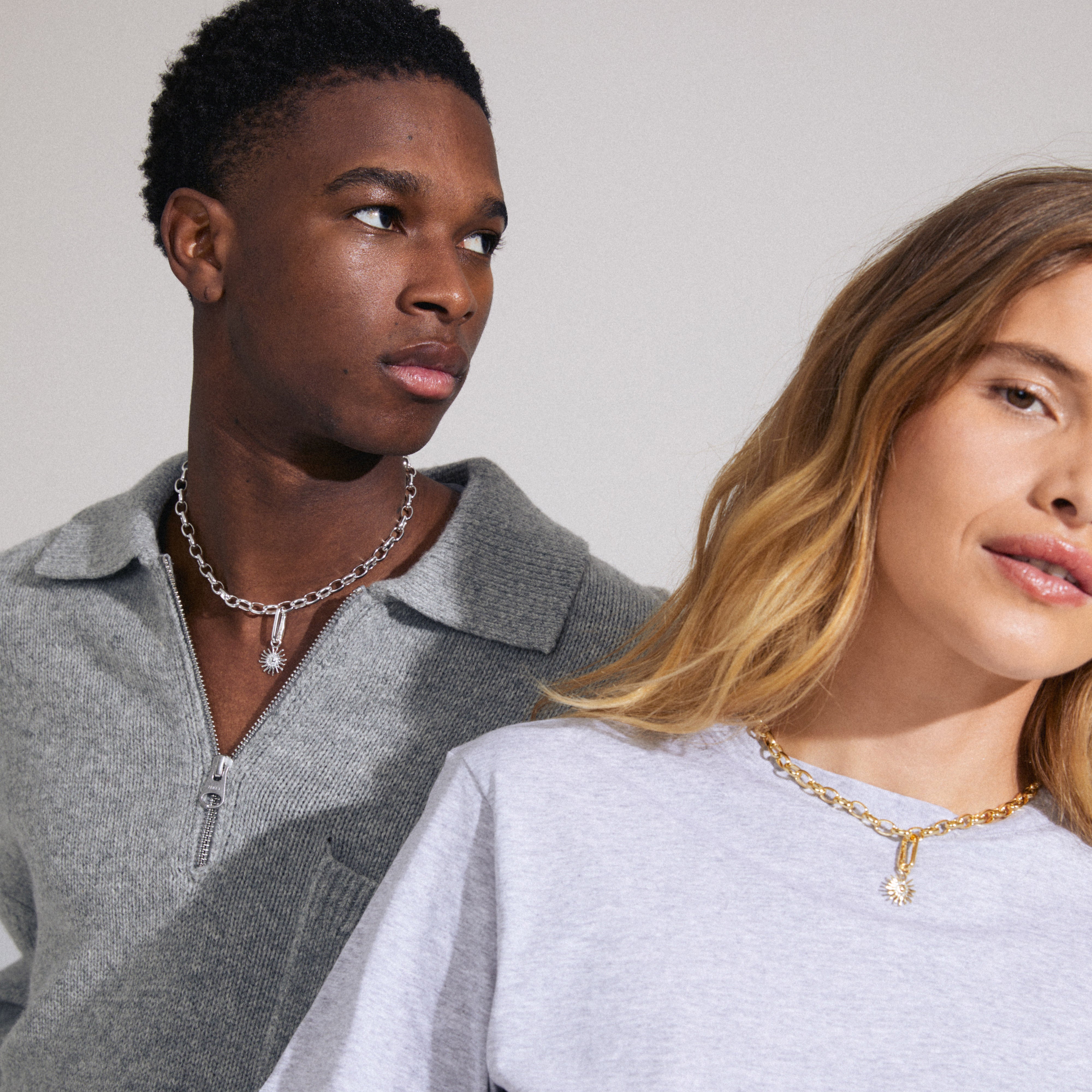 A man wearing Pilgrim's CHARM sun pendant, silver-plated, with Preciosa crystals, showcasing its elegant design against a grey sweater in a stylish pose.