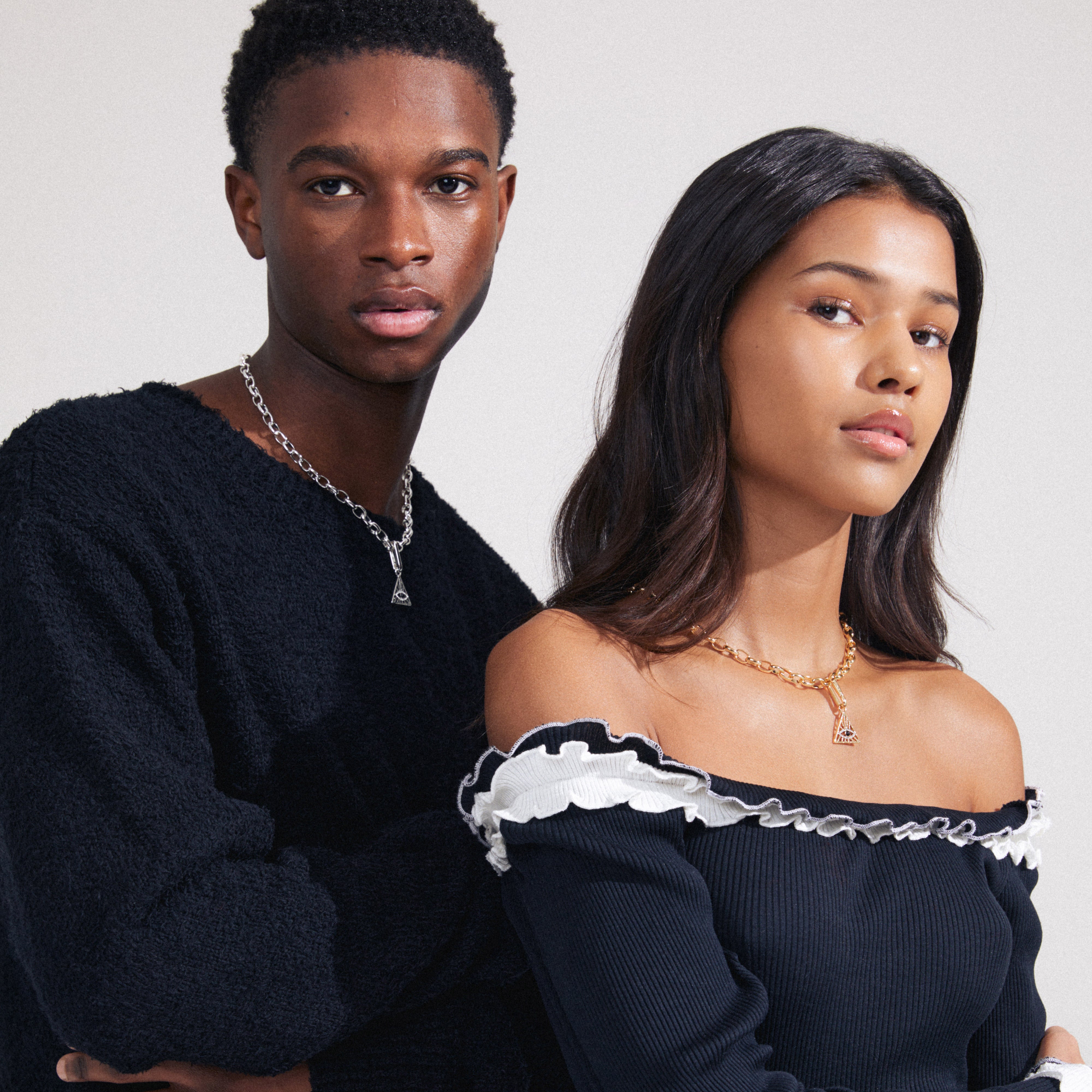 A man and woman pose, highlighting a CHARM triangle pendant, silver-plated, with an all-seeing eye, worn by the woman, symbolizing personalized style.