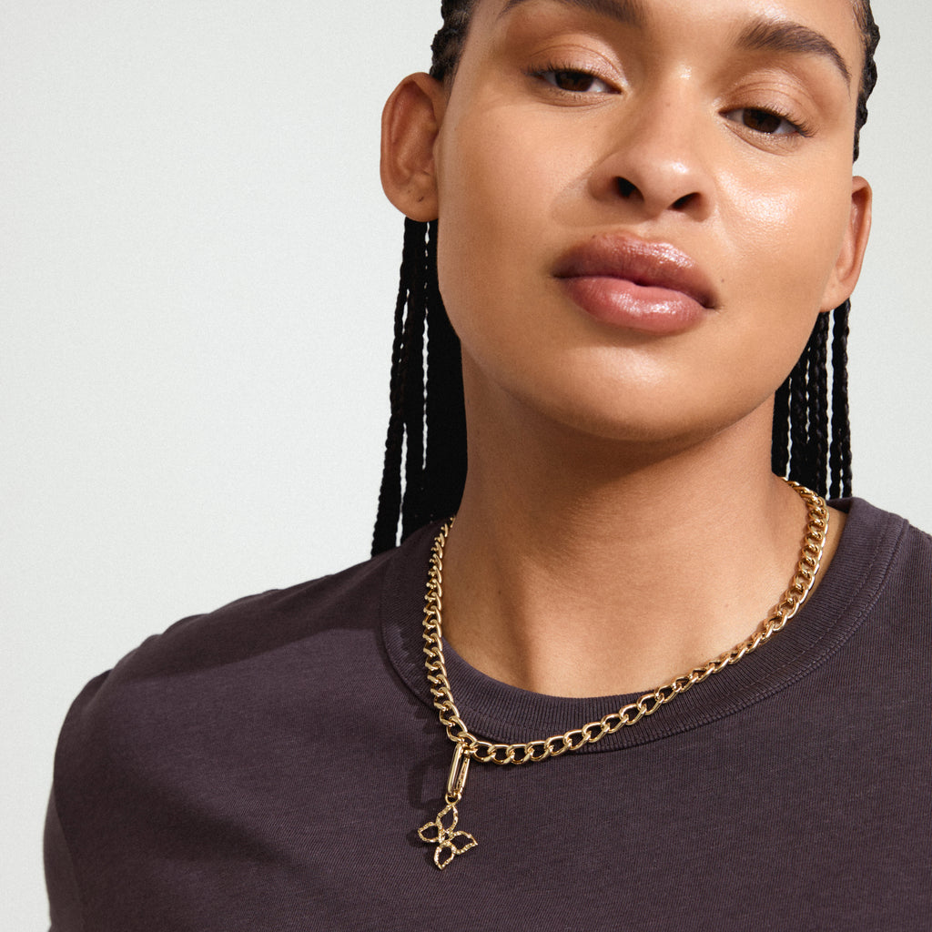 Woman with braids wears Pilgrim's CHARM butterfly pendant, gold-plated and adorned with Preciosa crystals, symbolizing transformation and freedom.