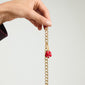 Gold-plated four-leaf clover pendant with red enamel, held by a hand, showcasing Pilgrim's playful, nature-inspired design ideal for personal style.