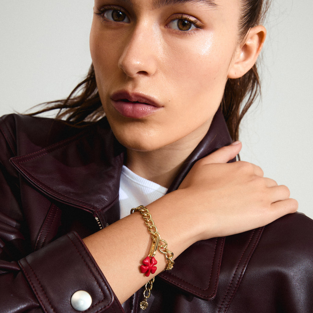 Woman wearing a leather jacket showcasing the CHARM clover pendant gold-plated by Pilgrim, featuring a red enamel finish and crafted from recycled materials.