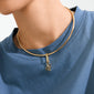 Close-up of a neck wearing Pilgrim's gold-plated CHARM f... pendant on a choker, showcasing edgy style with a small, stacked letter charm.