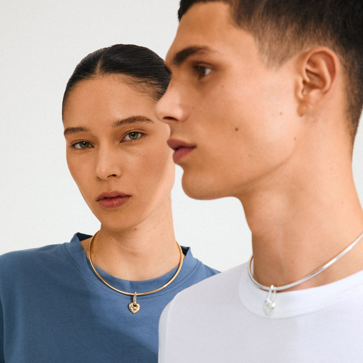 Two models showcase Pilgrim's CHARM rough heart pendant; the woman wears a gold-plated choker, highlighting minimalist, recycled jewelry for a personal touch.