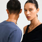 Models wearing minimalist metal chokers: woman in gold with a knot clasp, man in silver with sphere ends, showcasing Pilgrim's CHARM curl pendant style.