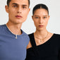 Two models showcase Pilgrim's CHARM bright pendant, gold-plated, featuring sunburst pendants; the woman wears gold with Tiger Eye, enhancing style and confidence.