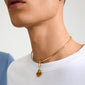 Close-up of Pilgrim's CHARM mold pendant: a gold-plated choker with an organic-shaped amber pendant, worn over a plain white T-shirt.