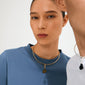 Two people showcasing Pilgrim's CHARM mold pendant, gold-plated with an amber acrylic stone, highlighting minimalist, bold, and eco-friendly Scandinavian design.
