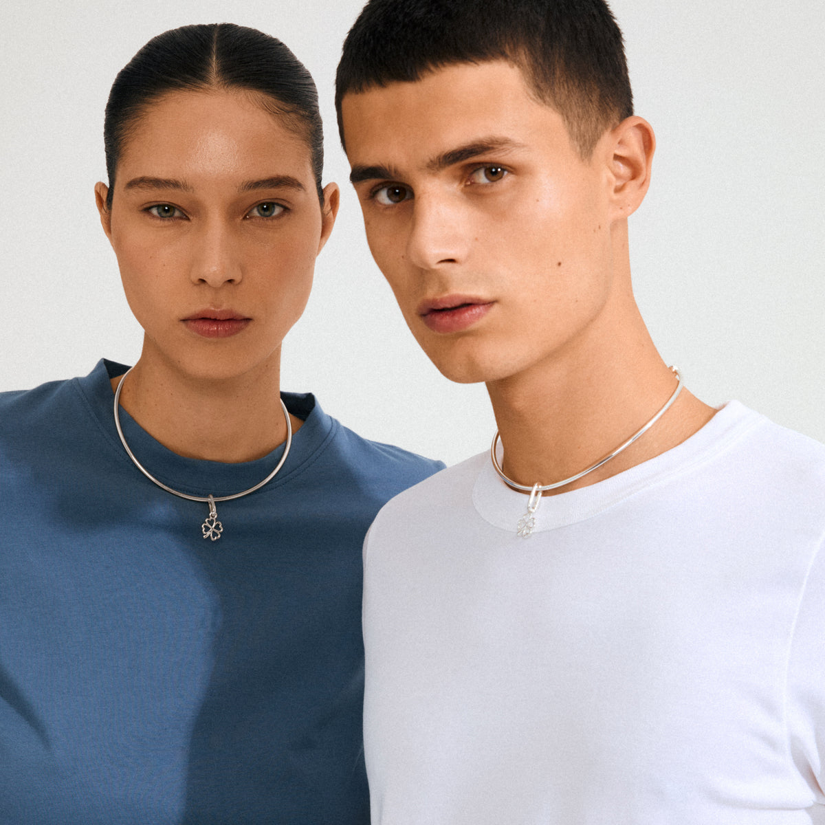 Models wearing Pilgrim's CHARM clover pendant, silver-plated, on smooth tubular chokers. The pendant adds a lucky, stylish touch to their minimalist outfits.