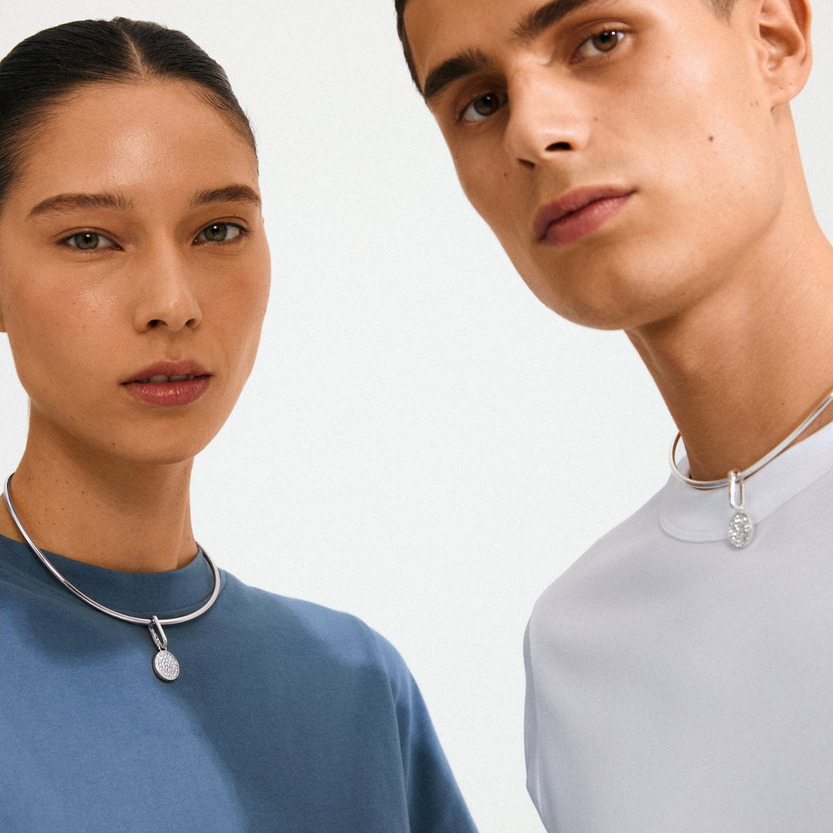 Models wearing Pilgrim's CHARM crystal coin pendant; a silver-plated necklace with sparkling crystals, highlighting personal style and sustainable fashion.