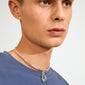 Person wearing Pilgrim's silver-plated CHARM curl pendant necklace with a simple blue shirt, showcasing a playful, artistic design and a small hoop earring.