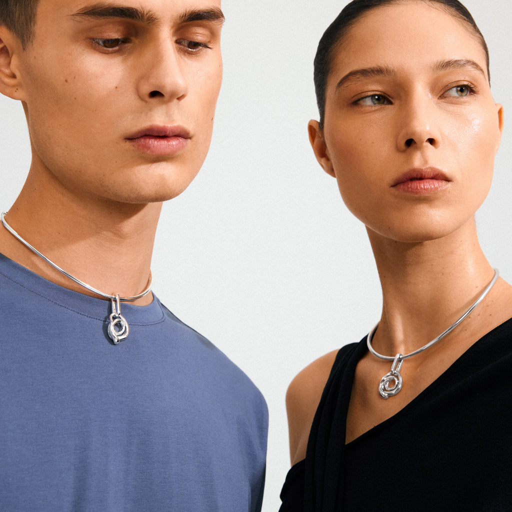 Models showcasing Pilgrim's CHARM curl pendant, silver-plated with a sculptural loop, emphasizing creative flair and sustainable fashion, complementing casual attire.