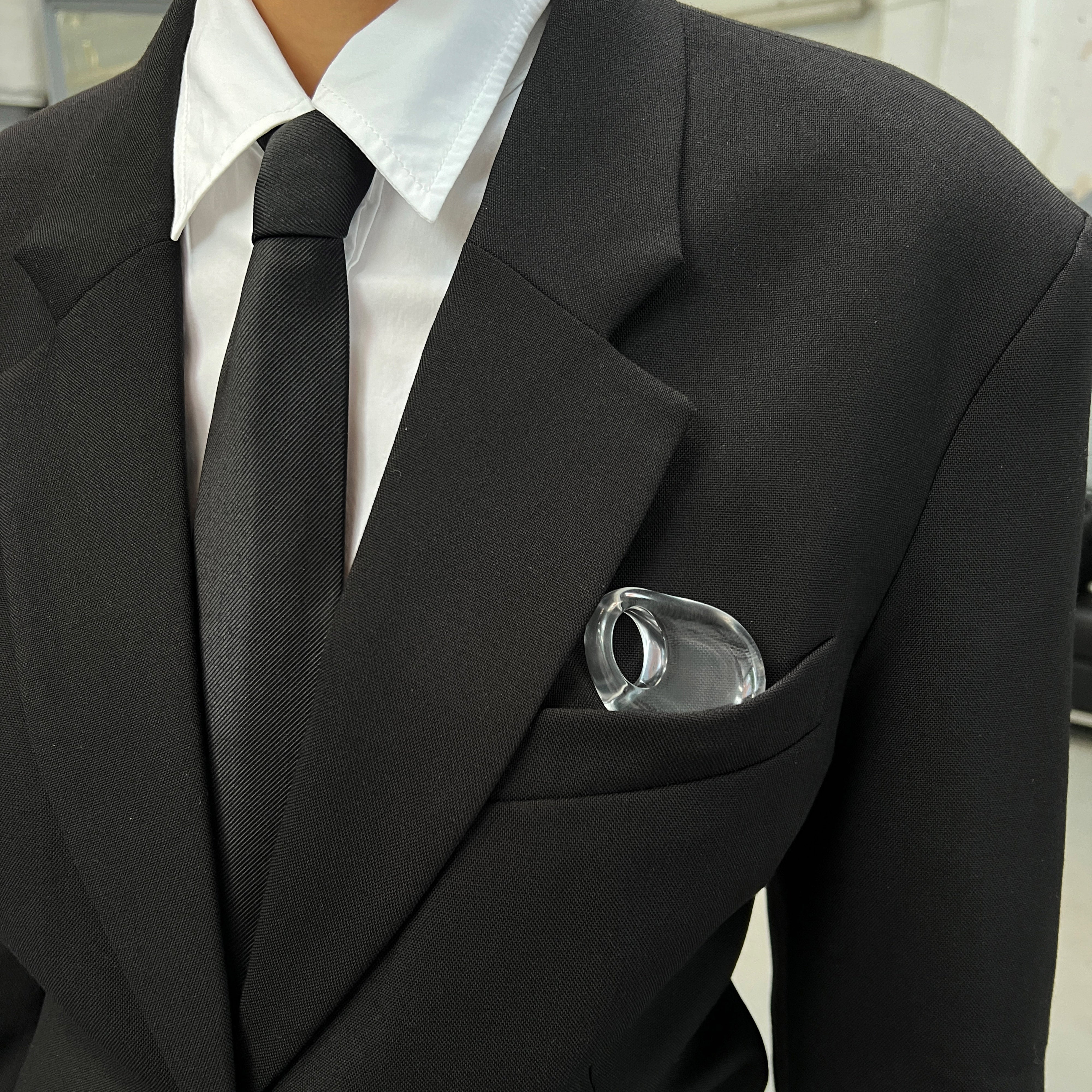 FREJA WEWER x PILGRIM Aqua necklace, crystal, prominently displayed in a black suit pocket, showcasing its modern hag stone design with a large, clear glass loop pendant.