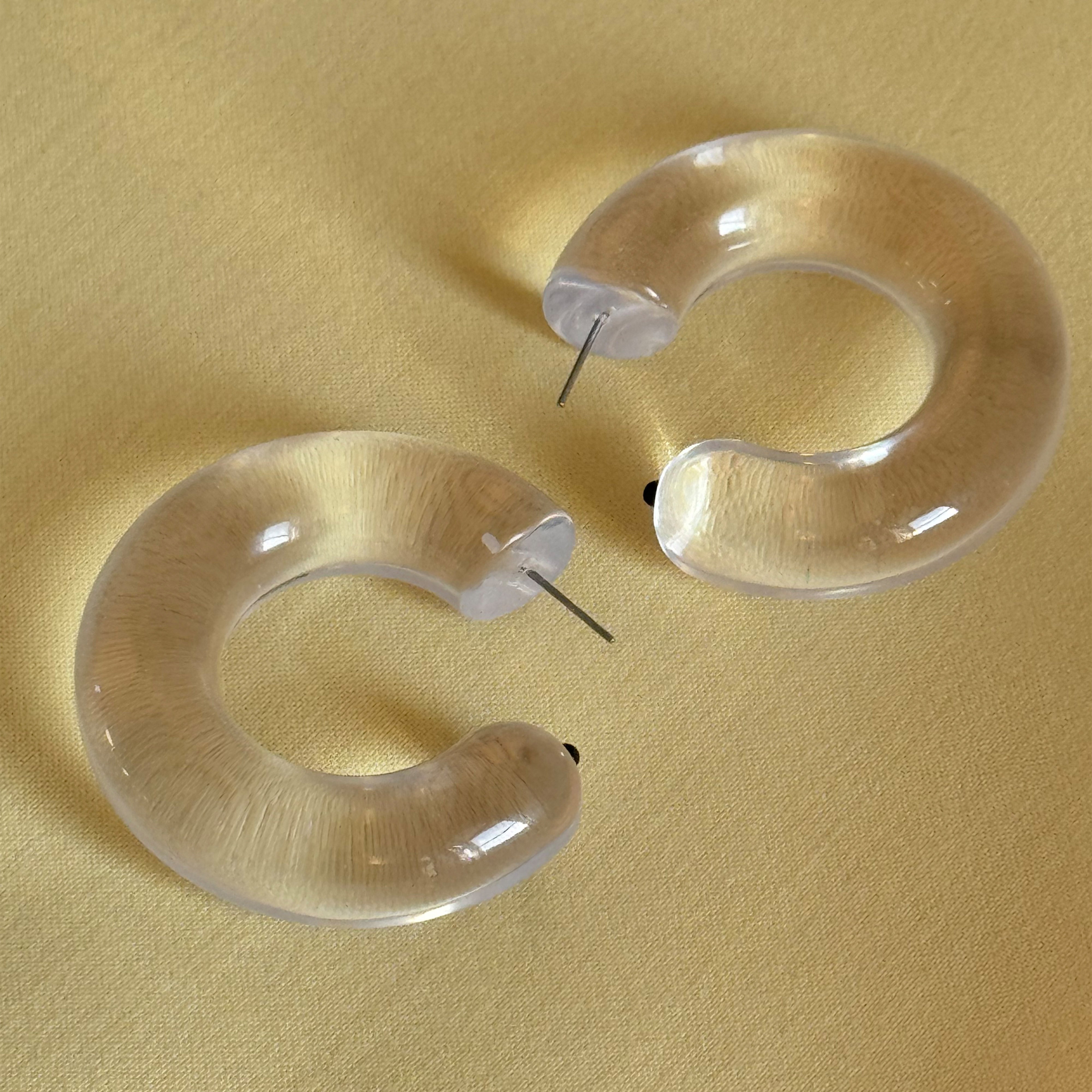 FREJA WEWER x PILGRIM Aqua hoops medium, crystal: Chunky, translucent crescent-shaped earrings with metal posts, offering a stylish, eco-friendly accessory made from recycled materials.