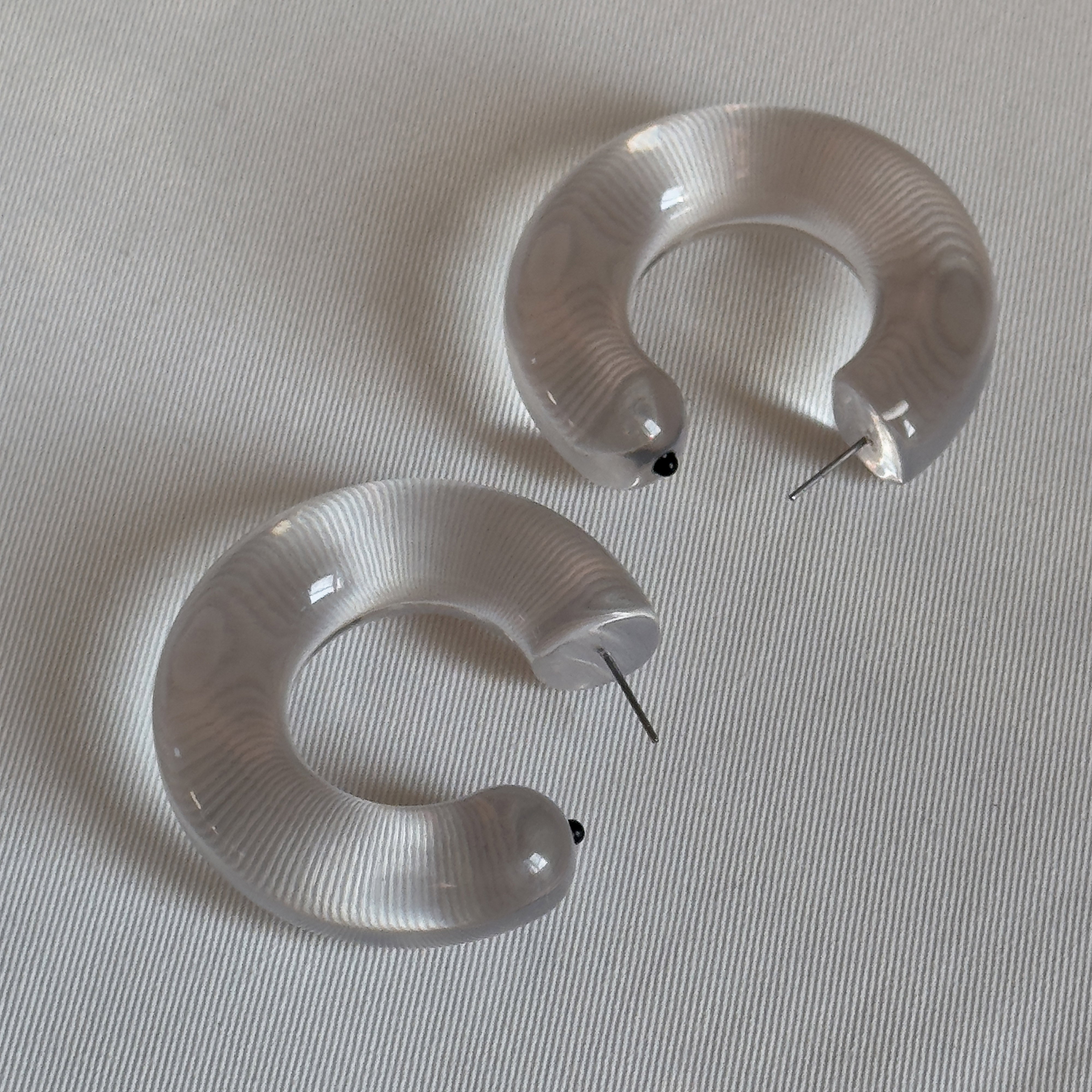 FREJA WEWER x PILGRIM Aqua hoops medium, crystal: Translucent crescent-shaped acrylic earrings with metal posts and black bead tips, offering trendy, eco-friendly style.