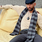 Man sitting on a couch wearing the FREJA WEWER x PILGRIM Polpo necklace with a large recycled black acrylic pendant on a fabric cord.