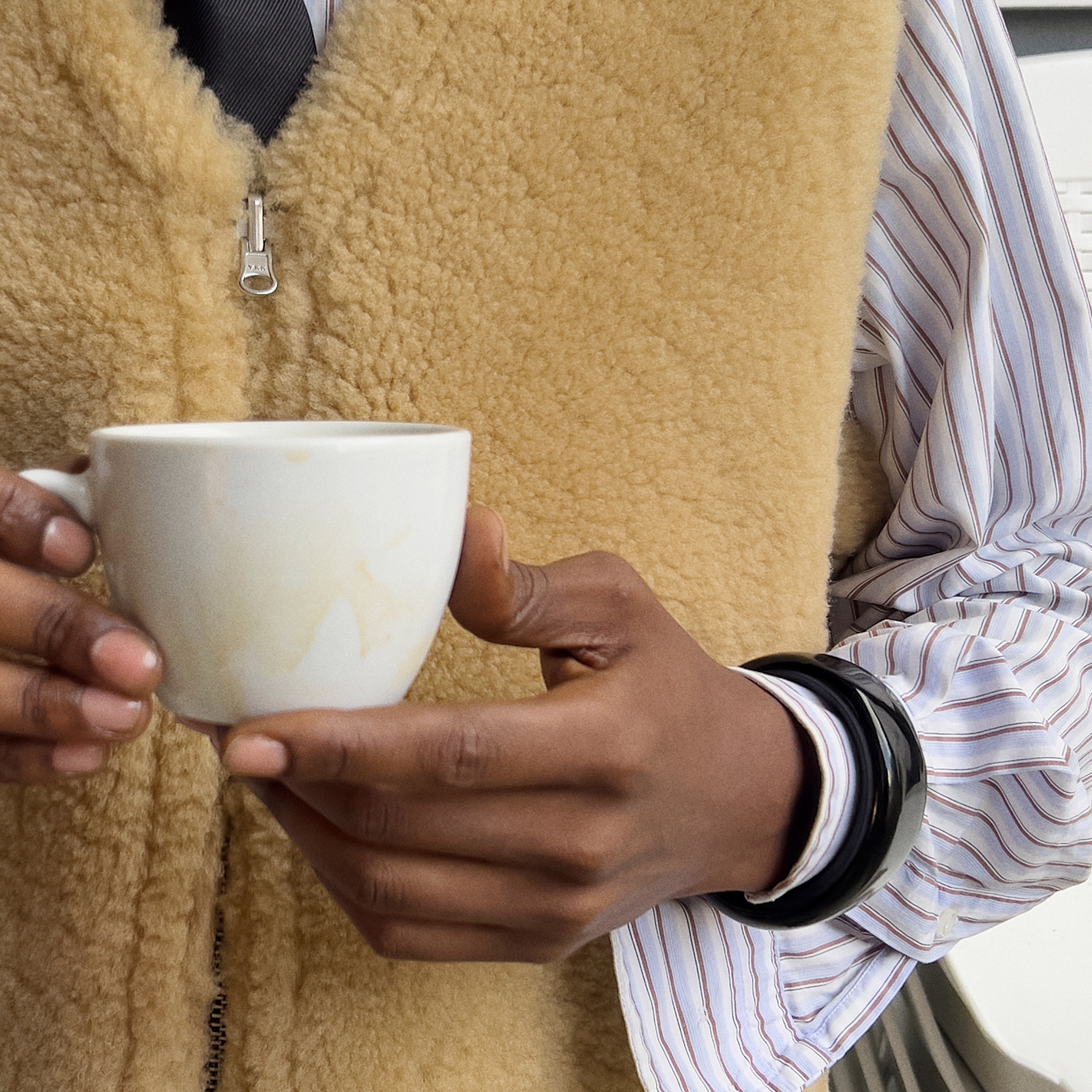 A person holds a white mug, wearing a black acrylic FREJA WEWER x PILGRIM Polpo bracelet, showcasing its chunky, sleek silhouette.
