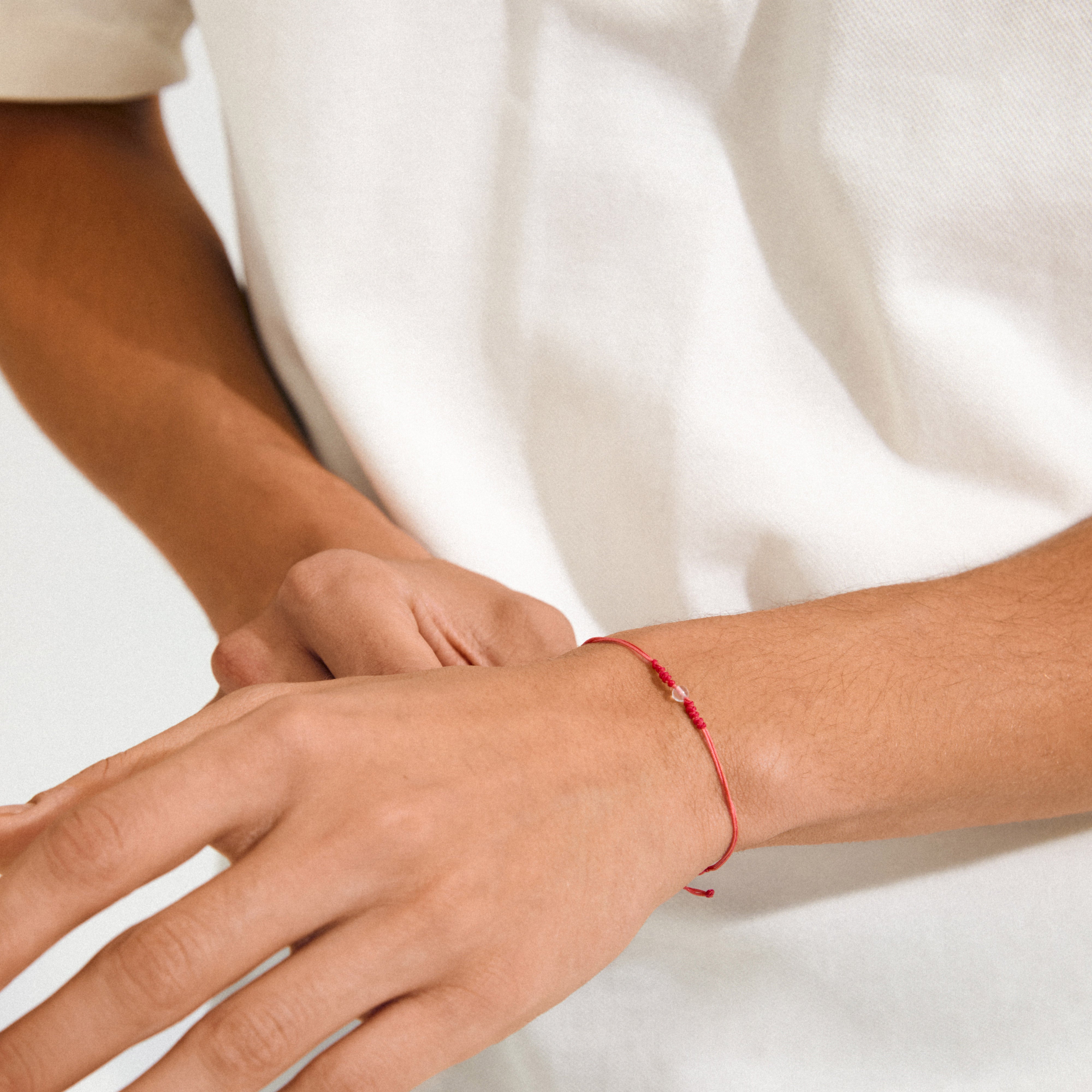 Close-up of a person's wrist wearing the APRIL birthstone bracelet, featuring a red cotton cord and a small Rock Crystal for minimalist style.
