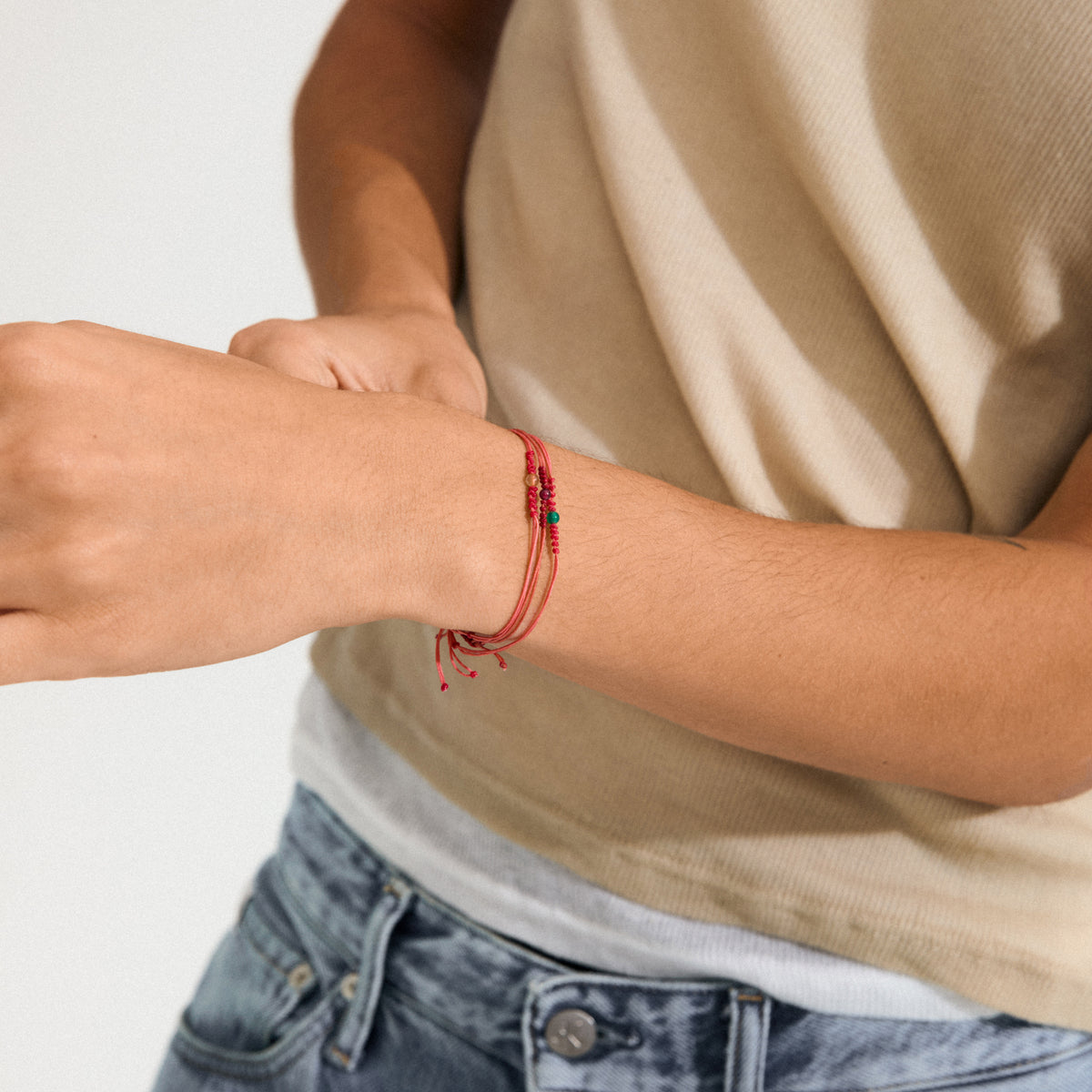 Close-up of a casual arm adorned with the JULY birthstone bracelet, featuring red cotton cord and a Red Agate bead, symbolizing courage and determination.