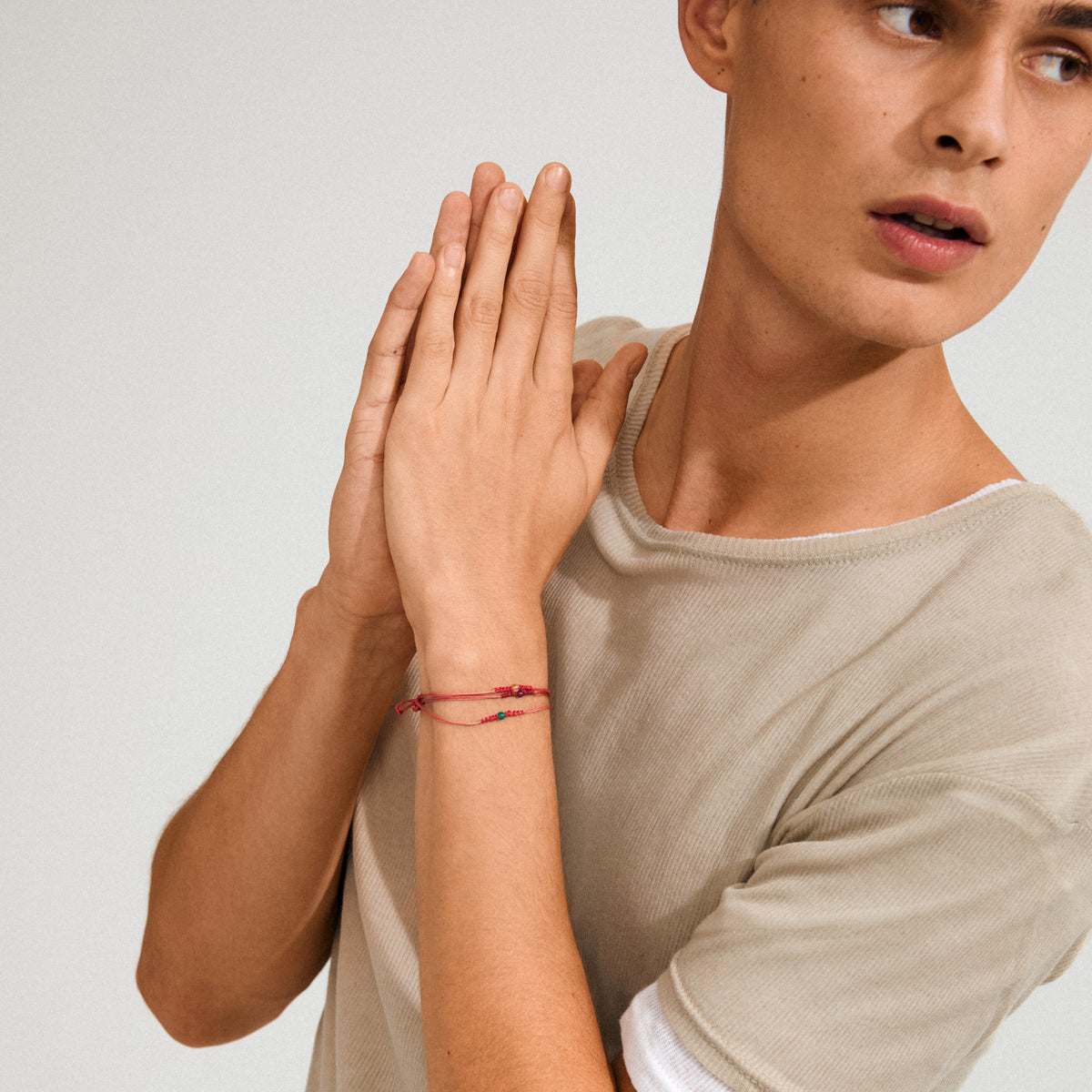 Young person wearing a MAY birthstone bracelet on left wrist, featuring red cord and a small Green Agate, symbolizing harmony and balance.