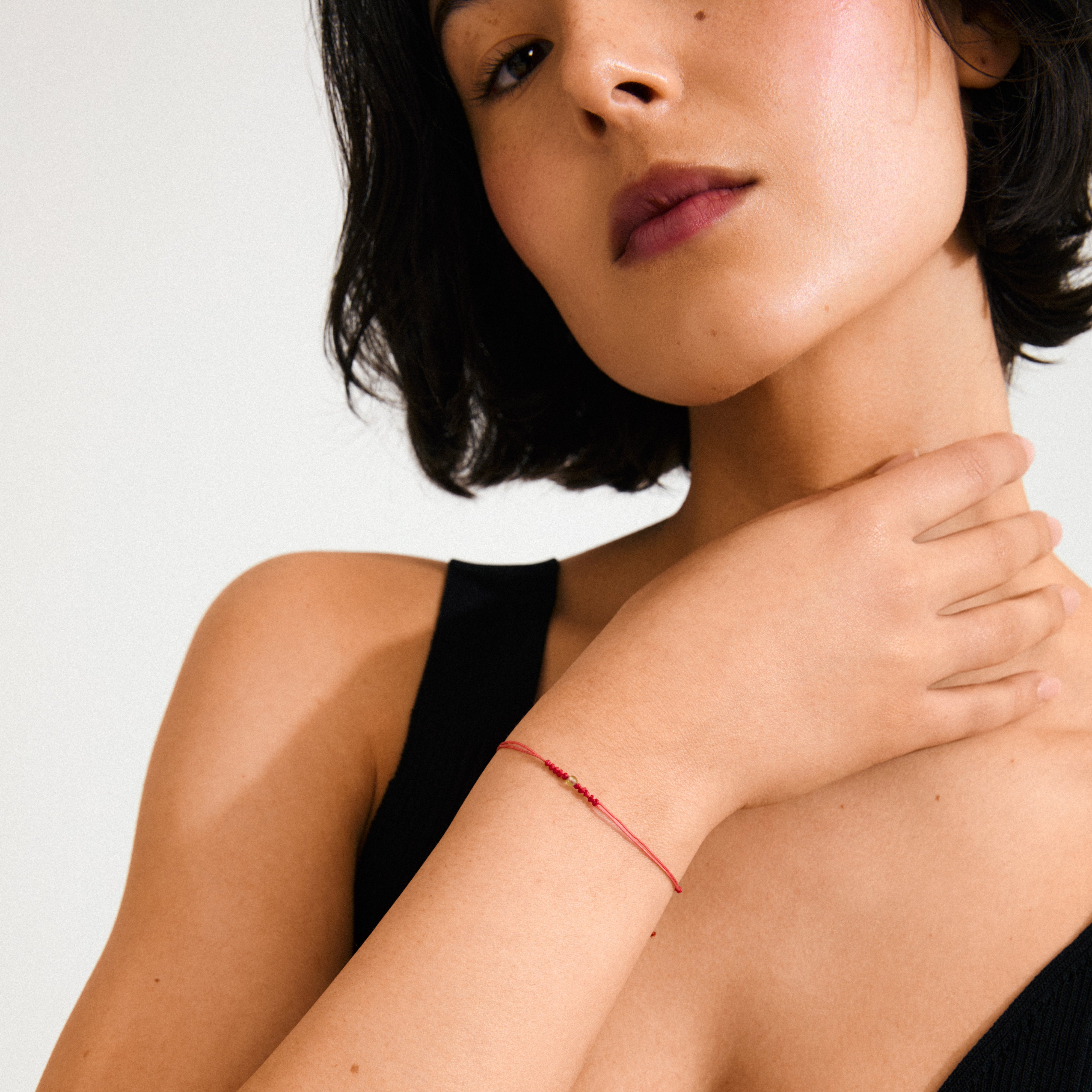 August birthstone bracelet featuring a red cotton cord with adjustable closure and a small Peridot gem, symbolizing happiness and joy.