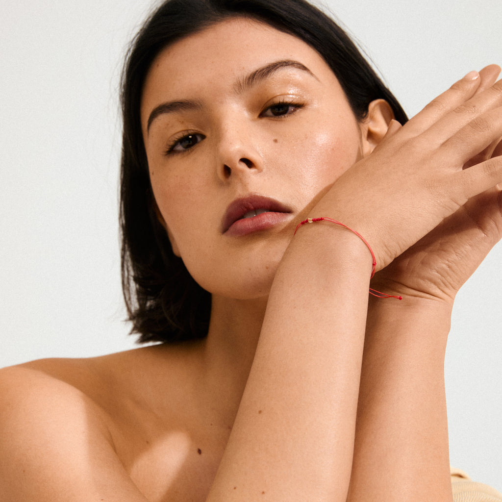 Woman wearing the NOVEMBER birthstone bracelet, featuring a red cotton cord and Topaz stone, symbolizing strength and determination, in a close-up pose.