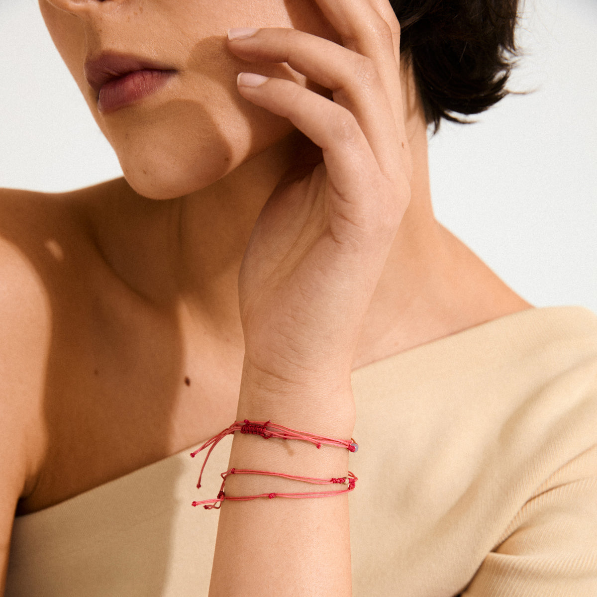 Woman wearing Pilgrim's NOVEMBER birthstone bracelet, a red cotton cord with an adjustable knot and Topaz, highlighting minimalist elegance against her beige off-the-shoulder top.