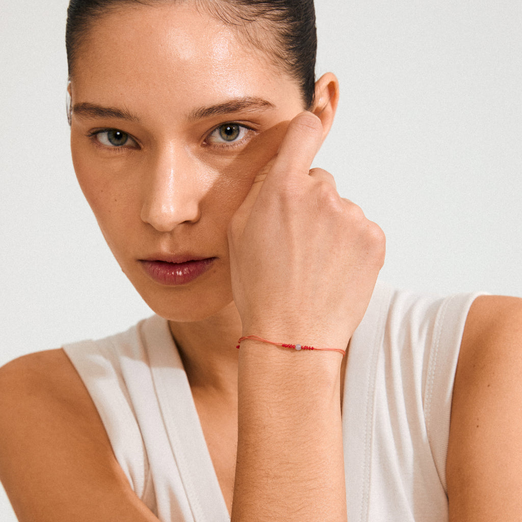 Woman showcasing the DECEMBER birthstone bracelet, featuring a delicate red cord and Blue Aventurine stone, symbolizing confidence and strength.