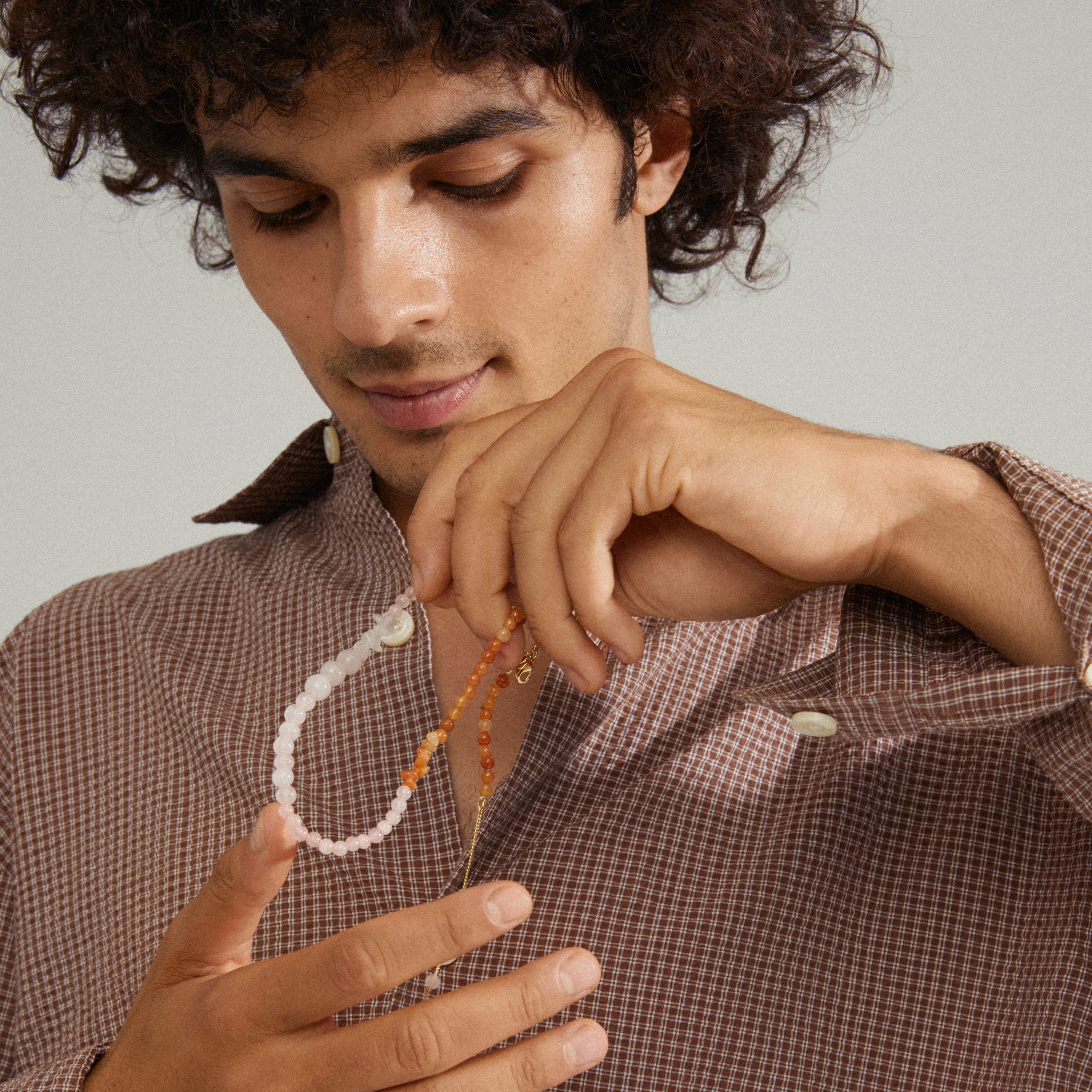 Man examining the SOULMATES necklace rose/gold-plated, featuring genuine rose quartz and red aventurine stones, symbolizing love and strength.
