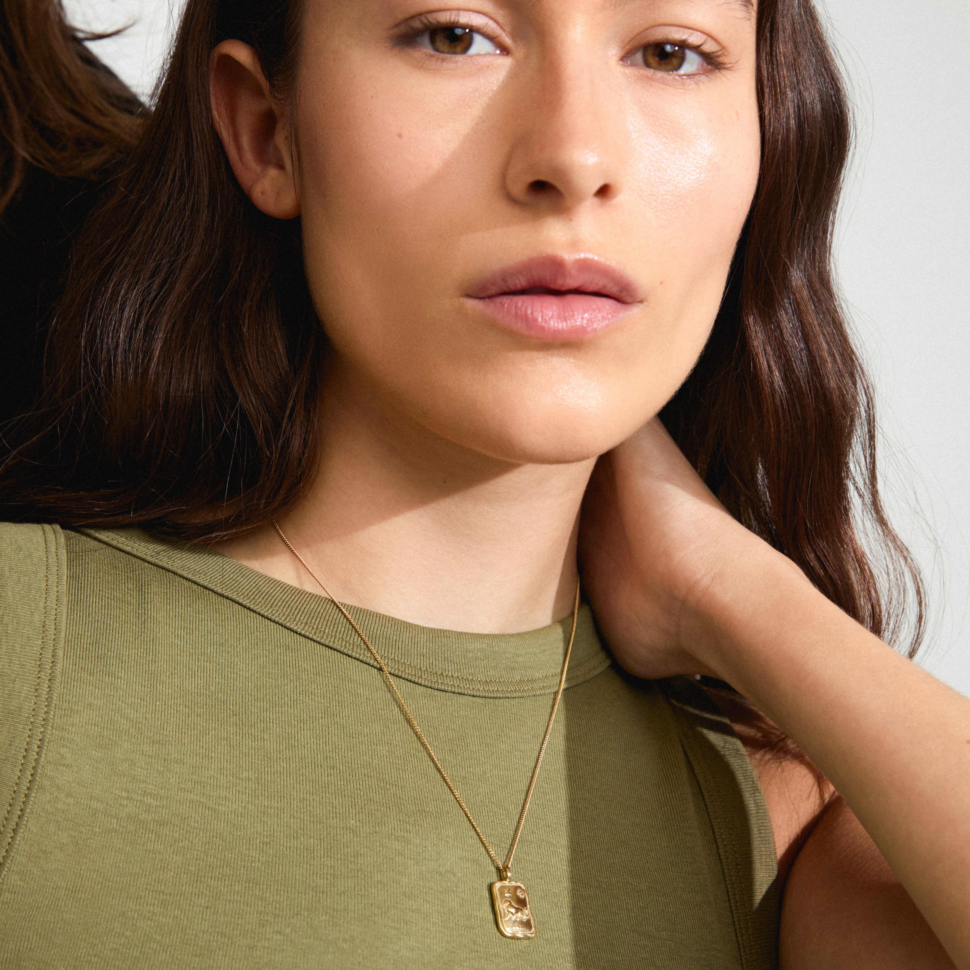 Woman wearing Pilgrim's LEO Zodiac Sign necklace, featuring a gold-plated chain with a reversible square coin pendant in a Leo motif and constellation design.
